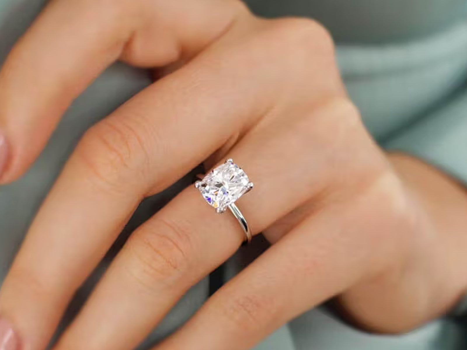 Close-up of a large cushion-cut or radiant-cut Moissanite engagement ring with a simple four-prong setting, worn on a finger