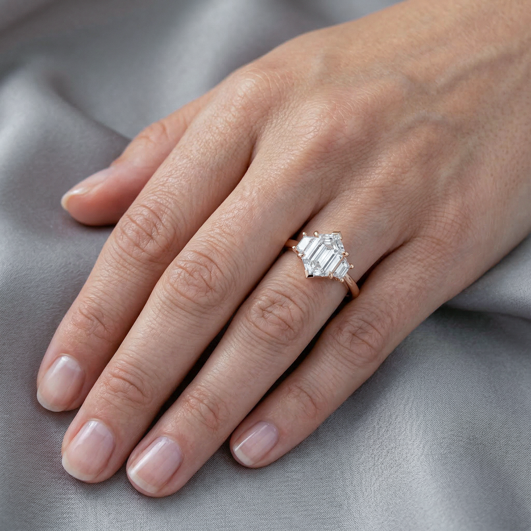 Hand wearing a hexagon cut diamond ring on a gray fabric background