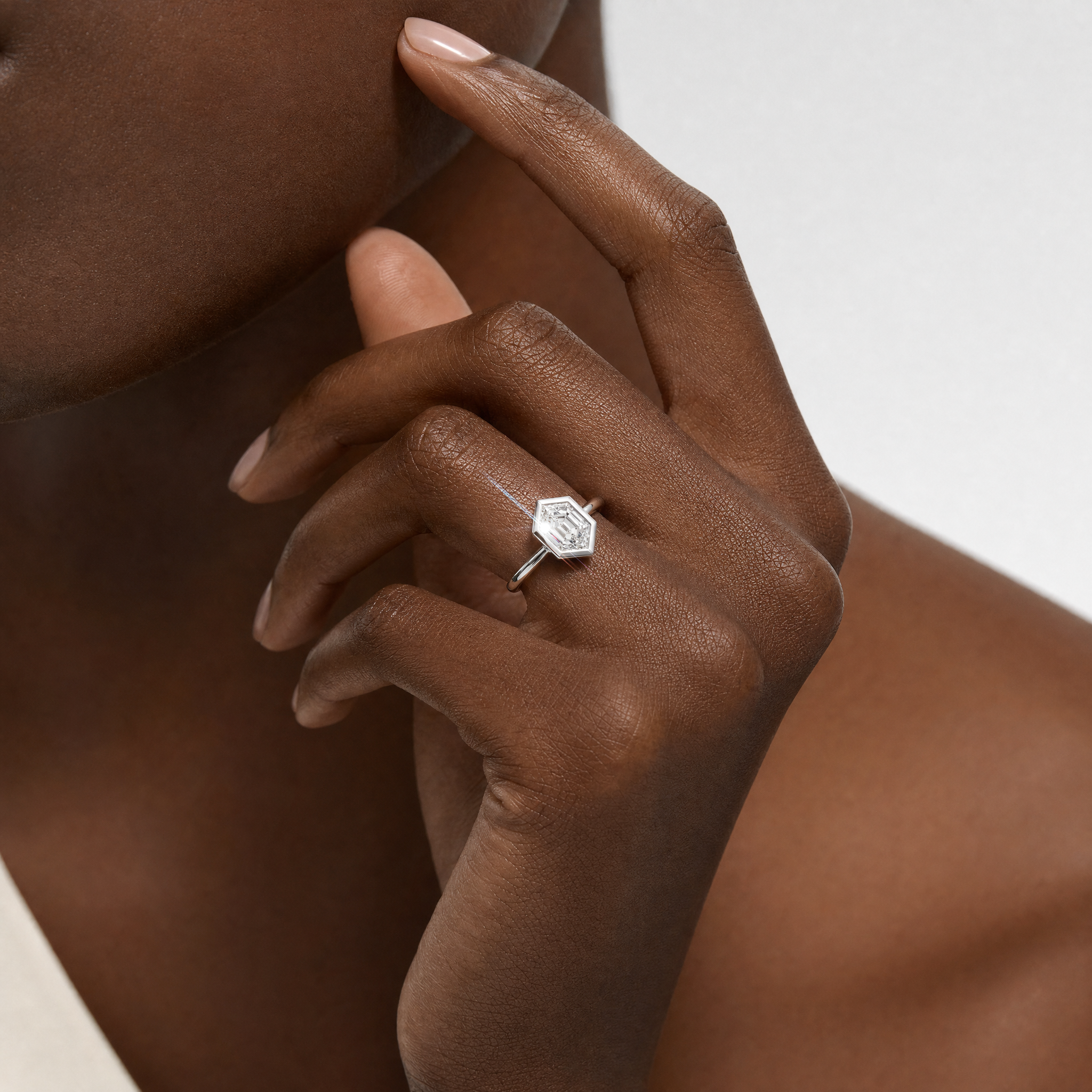 Close-up of a hand wearing a bezel setting hexagon shape diamond ring with a white background