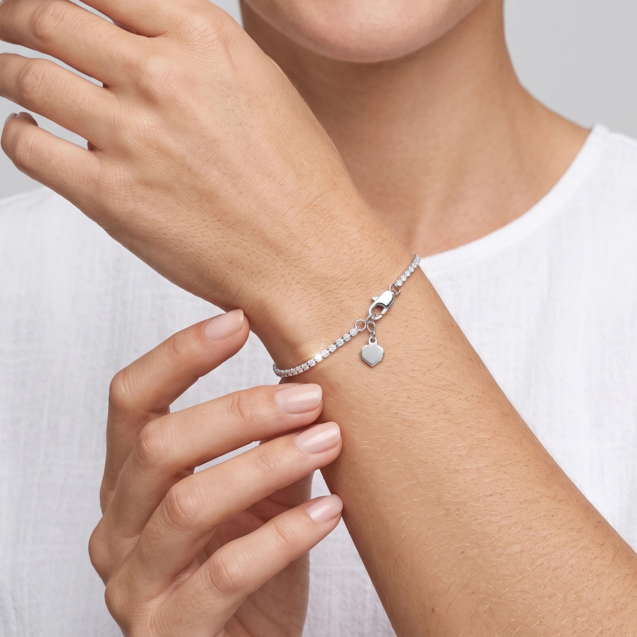 Close-up of a white gold lab-grown diamond tennis bracelet with an adjustable chain and heart charm.