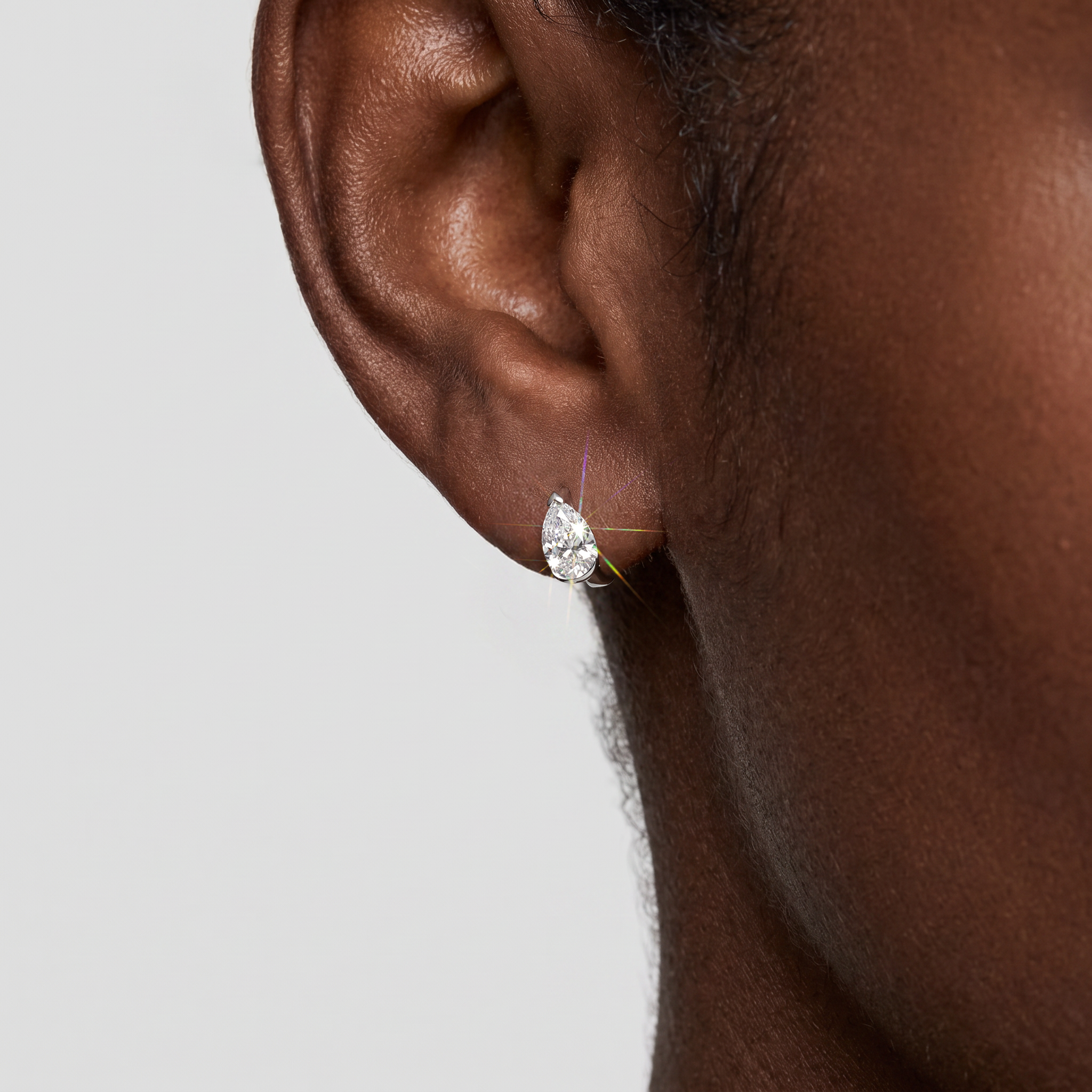 White-gold pear-shaped hoop earring worn on an ear in a close-up model view.
