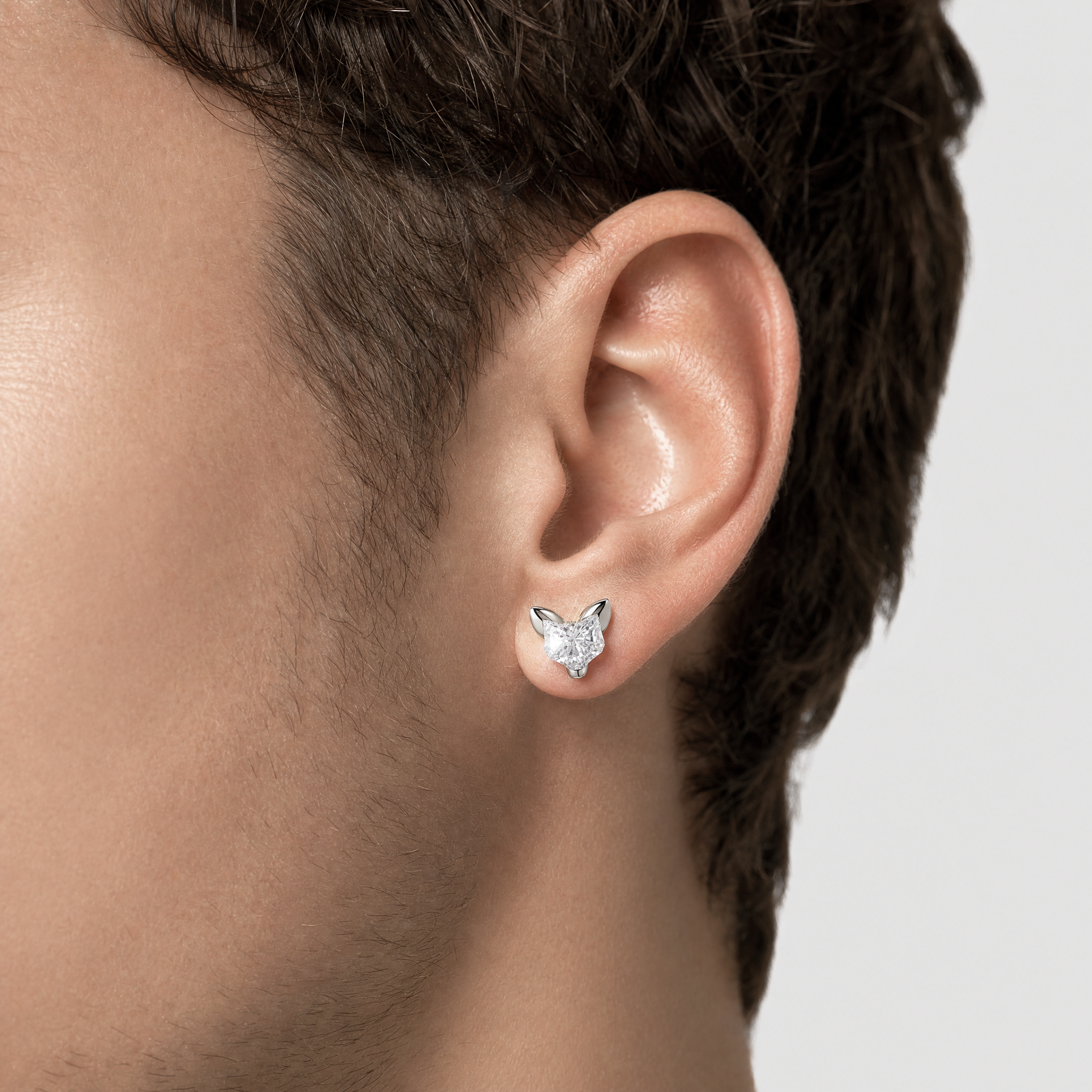 Close-up of an ear wearing a cat -shape diamond earring on a neutral background