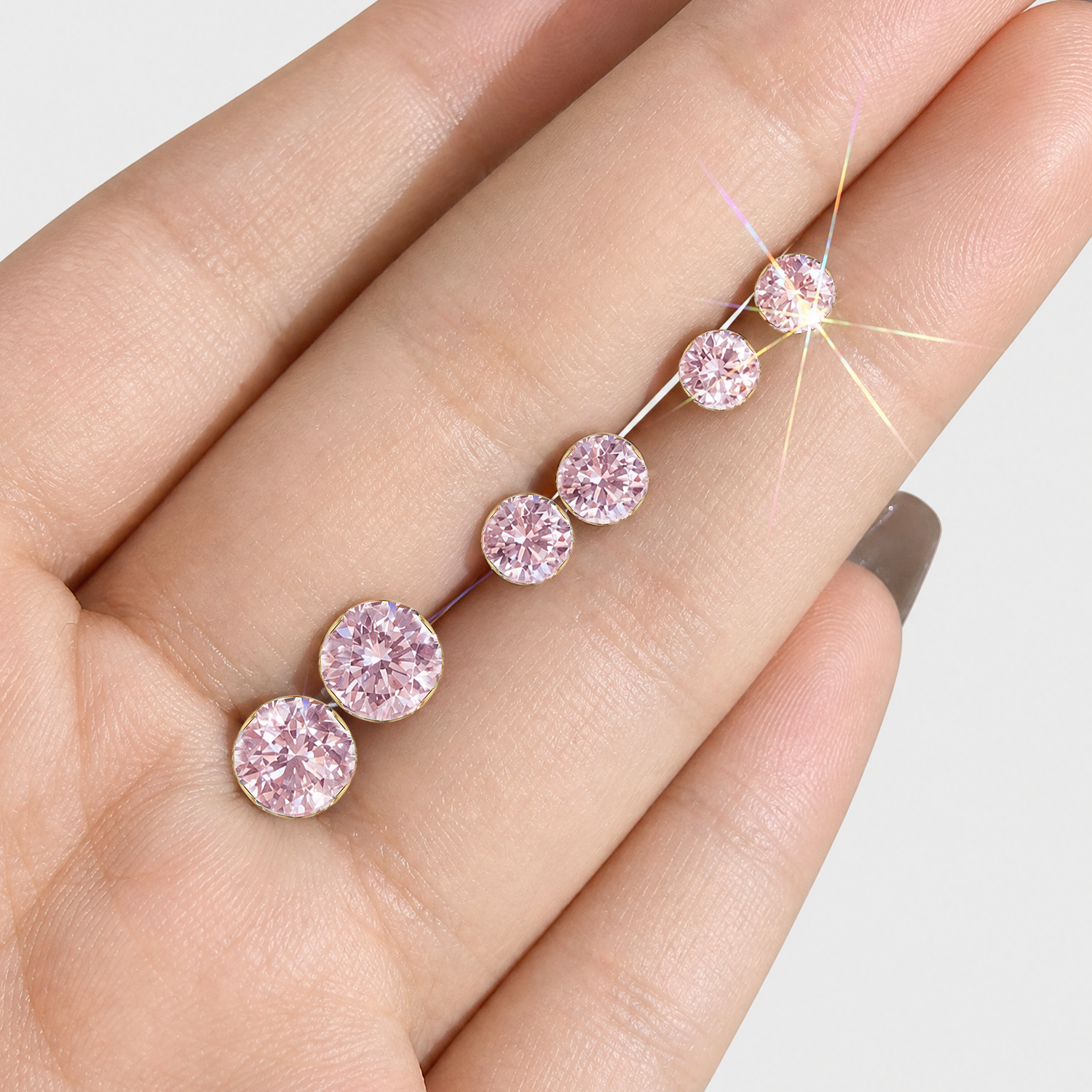 Round pink lab-grown diamond stud earrings in graduated sizes displayed on a hand.