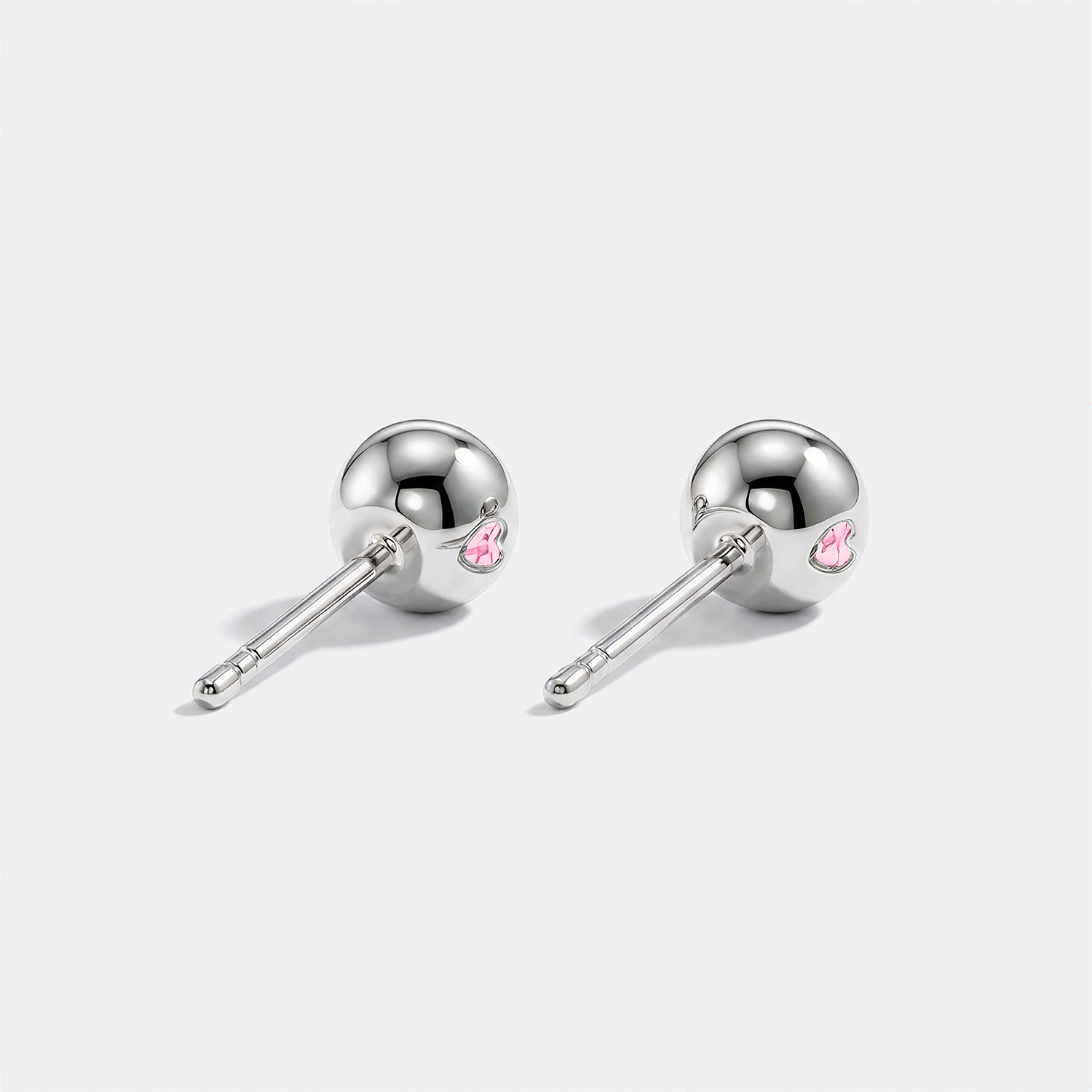 Back view of white gold stud earrings showing polished ball backs and small pink heart details.