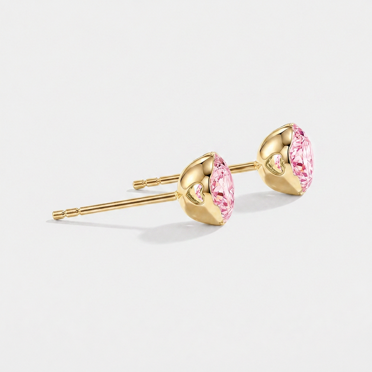 Side view of round pink lab-grown diamond stud earrings showing heart-shaped openings in the yellow gold settings.