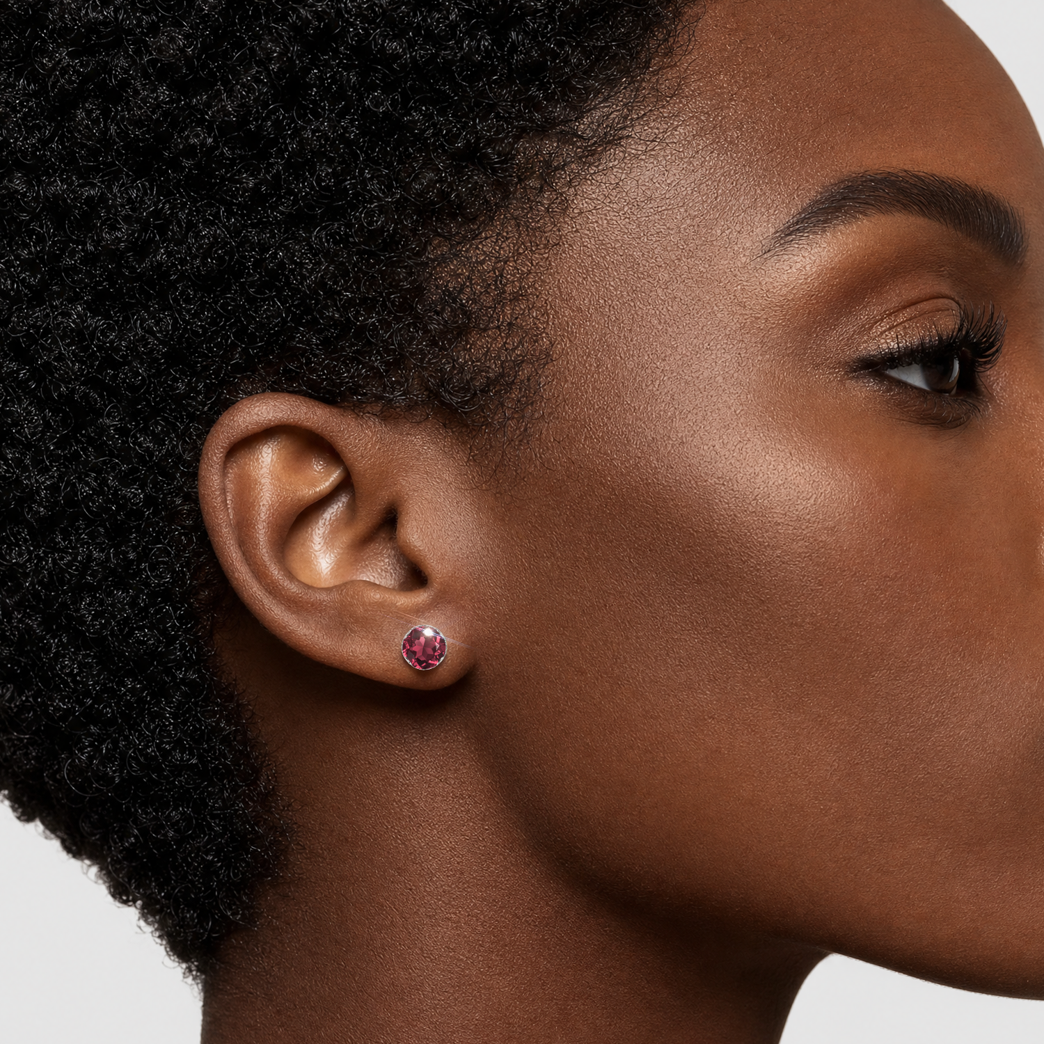 Two sizes of round lab-grown ruby stud earrings in white gold worn together on the ear.