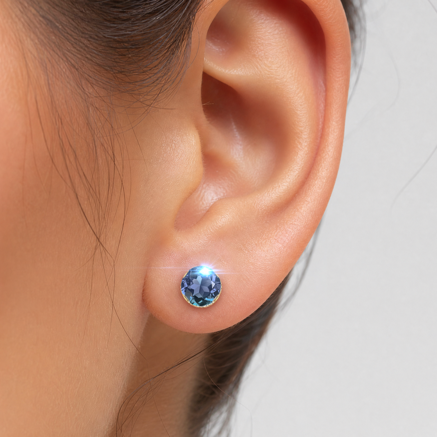 Close-up of a round lab-grown alexandrite stud earring in yellow gold worn on the earlobe.