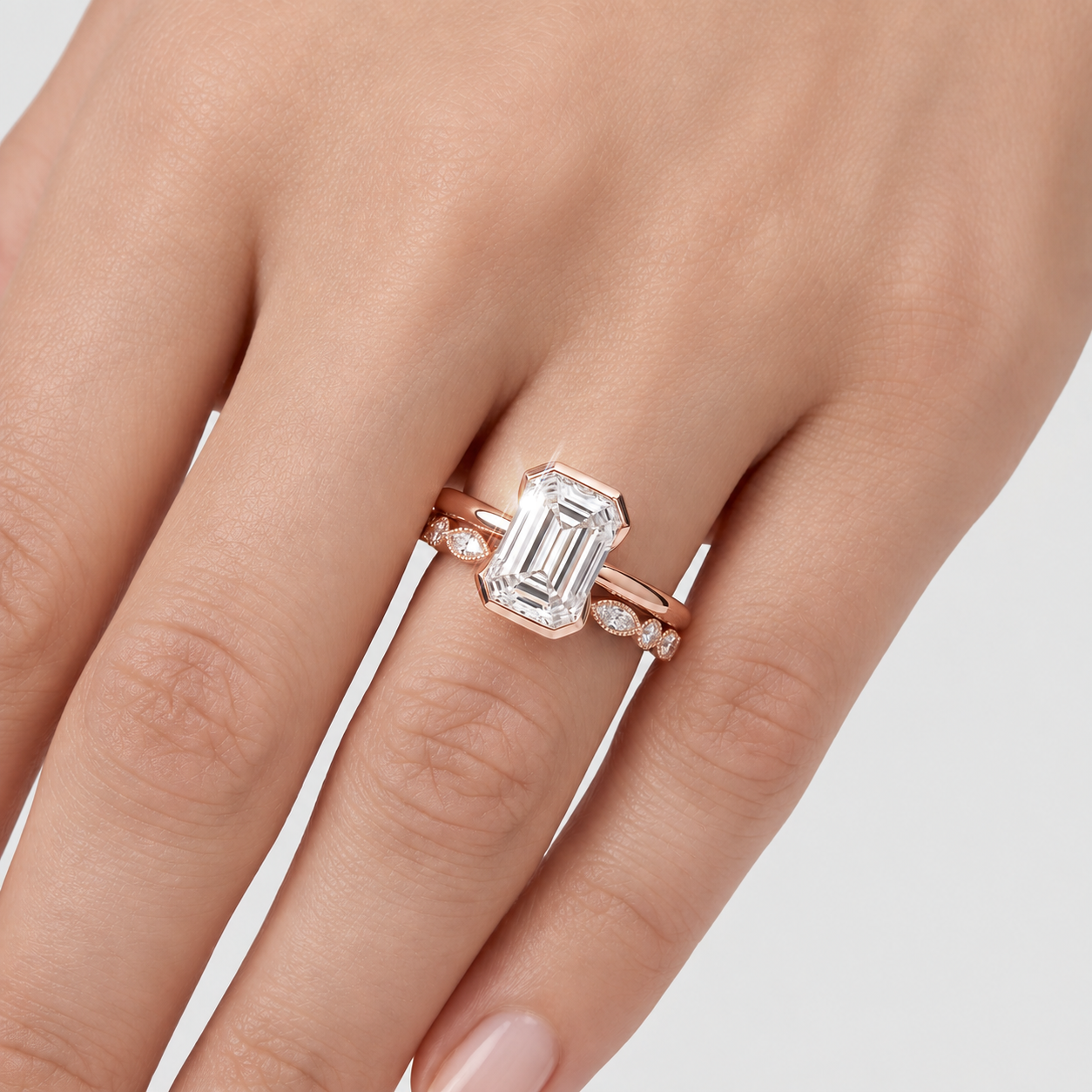 Close-up of an emerald-cut two-ring bridal set in rose gold worn on a hand.