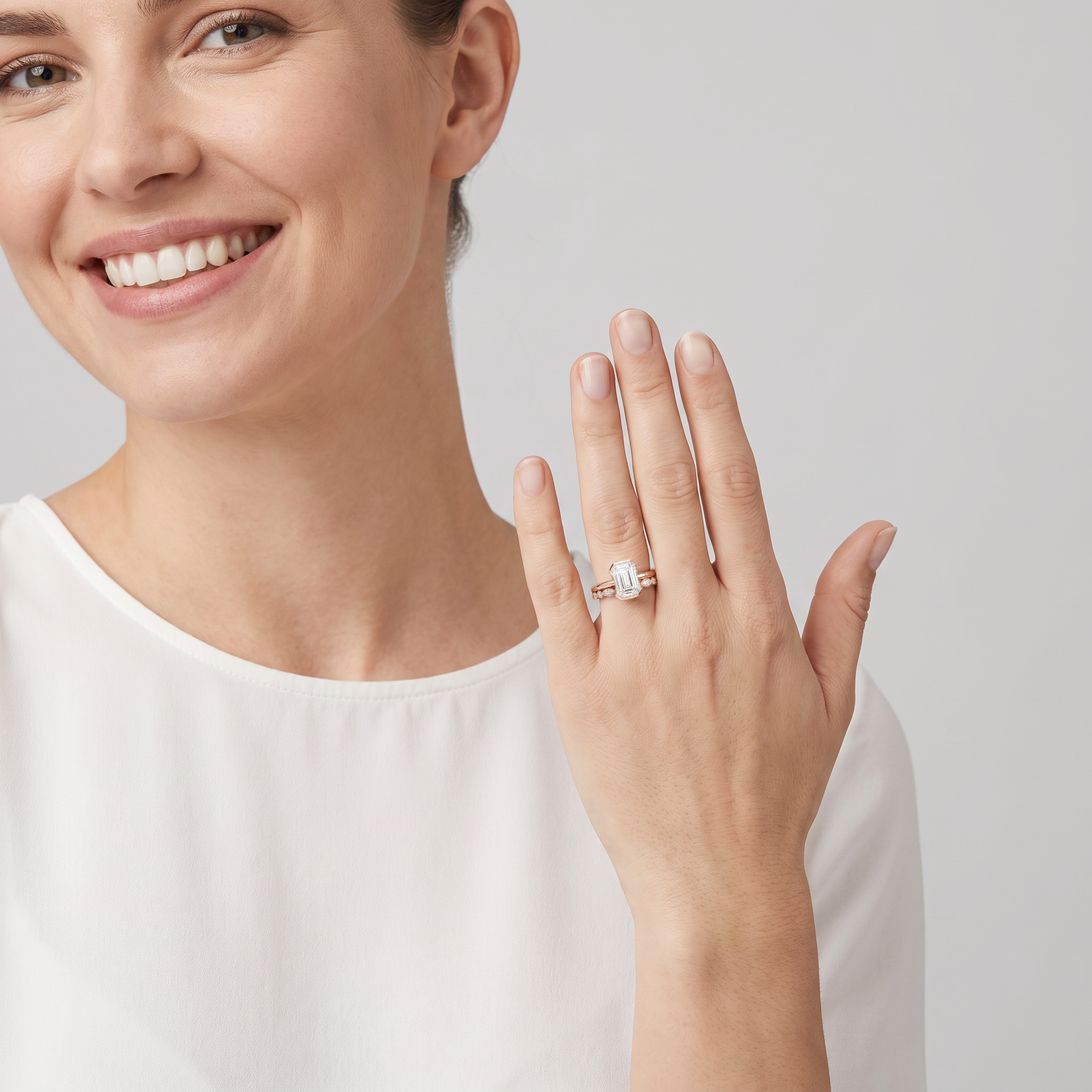 Model wearing an emerald-cut two-ring bridal set in rose gold on her raised hand.
