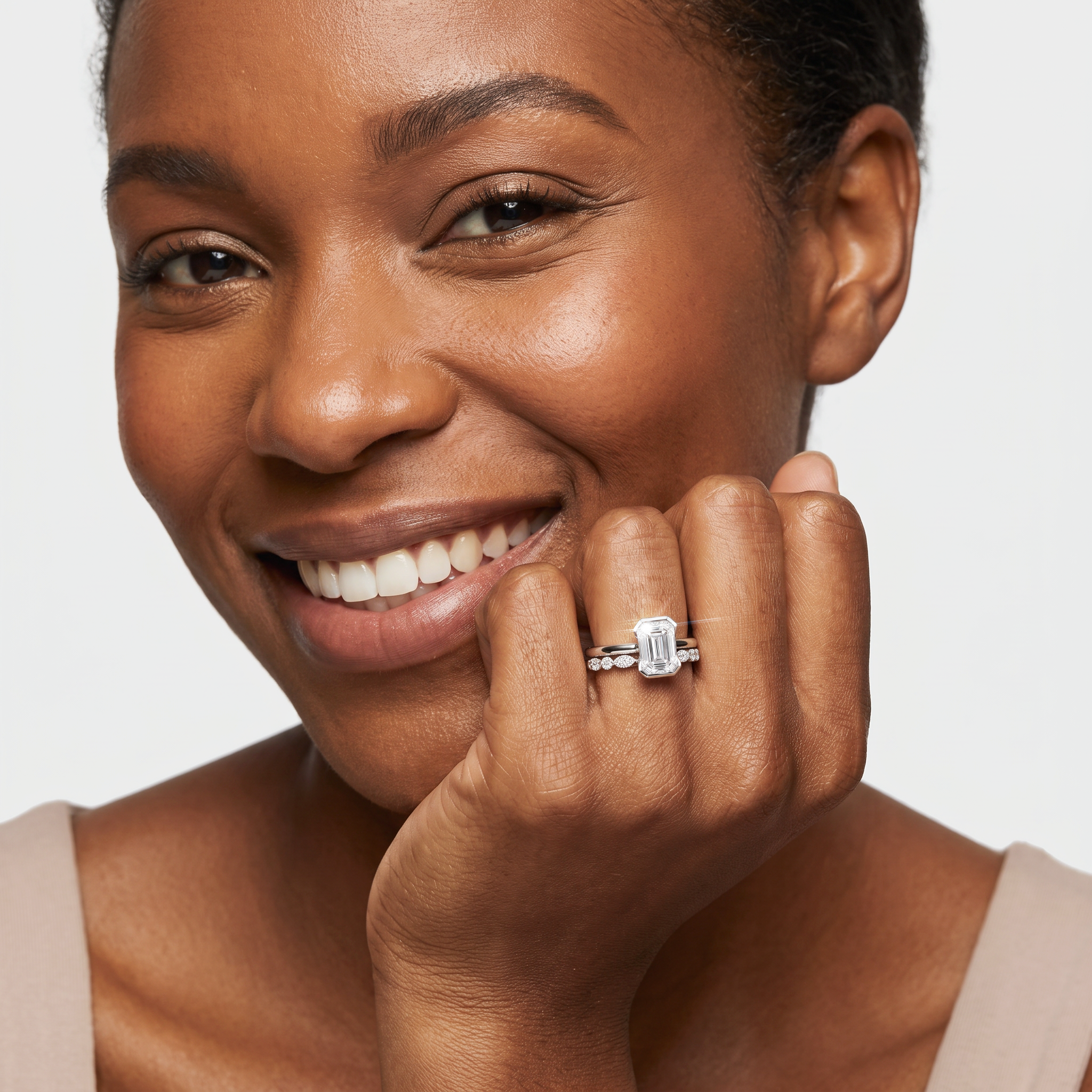 Model wearing an emerald-cut two-ring bridal set in white metal on her hand near her face.