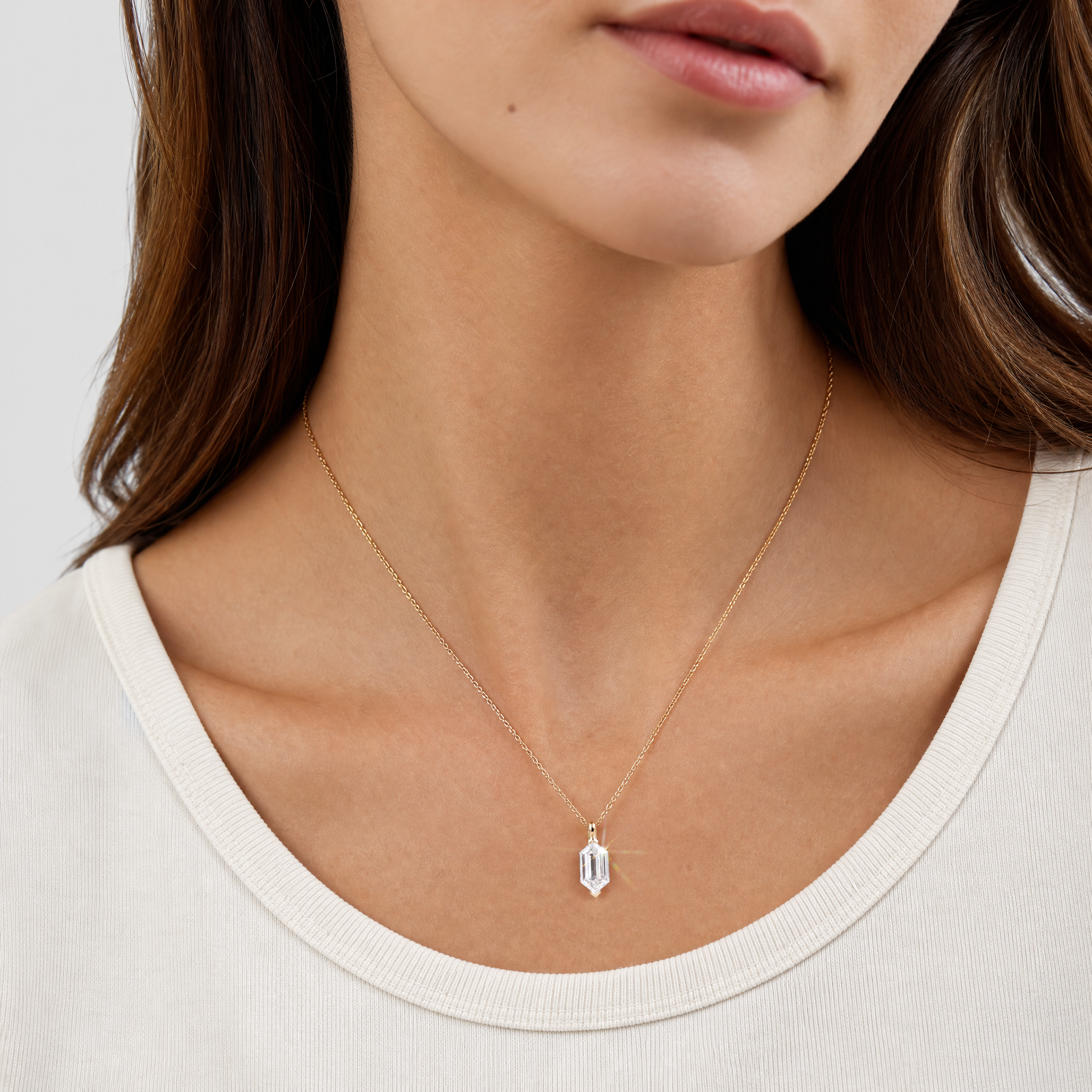 Yellow metal elongated hexagon-cut diamond pendant worn on the neck to show its scale.