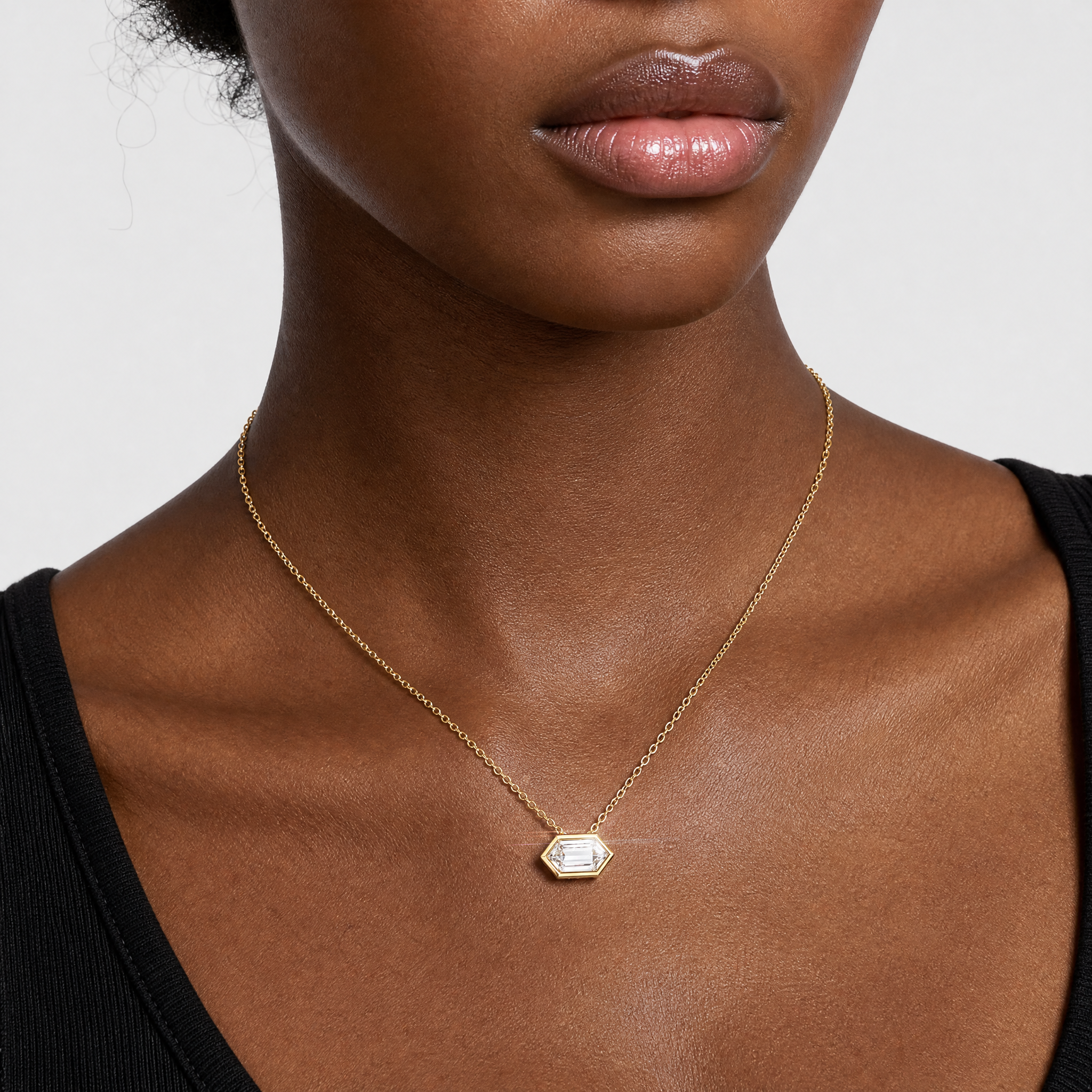 Model wearing an elongated hexagon-cut diamond pendant in yellow gold on a fine chain.