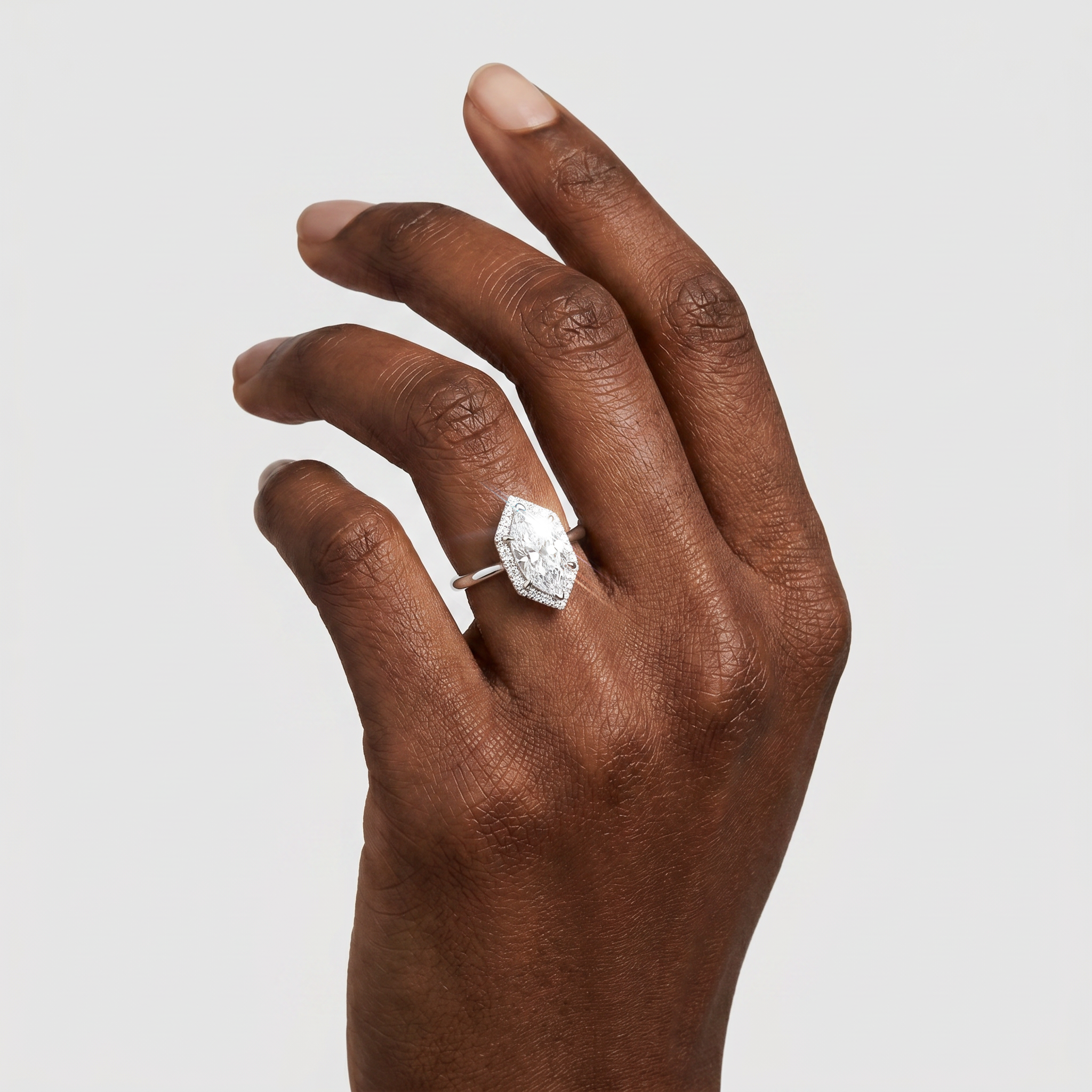 Hand wearing a halo hexagon diamond ring on a light gray background