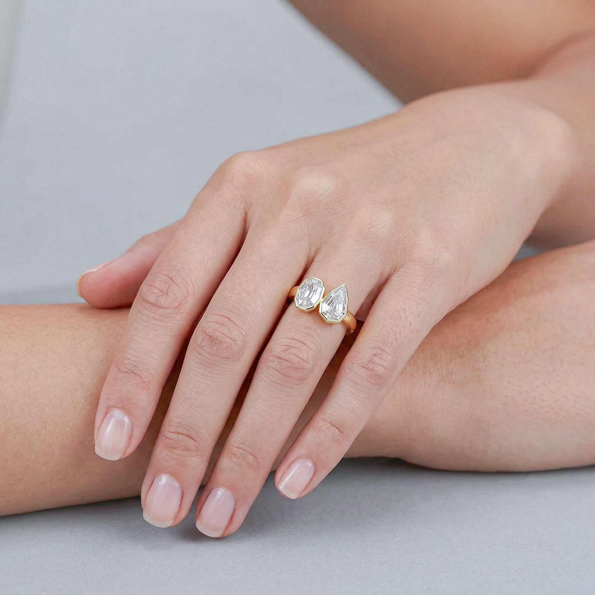 Hand wearing a golden ring with two diamonds on a neutral background