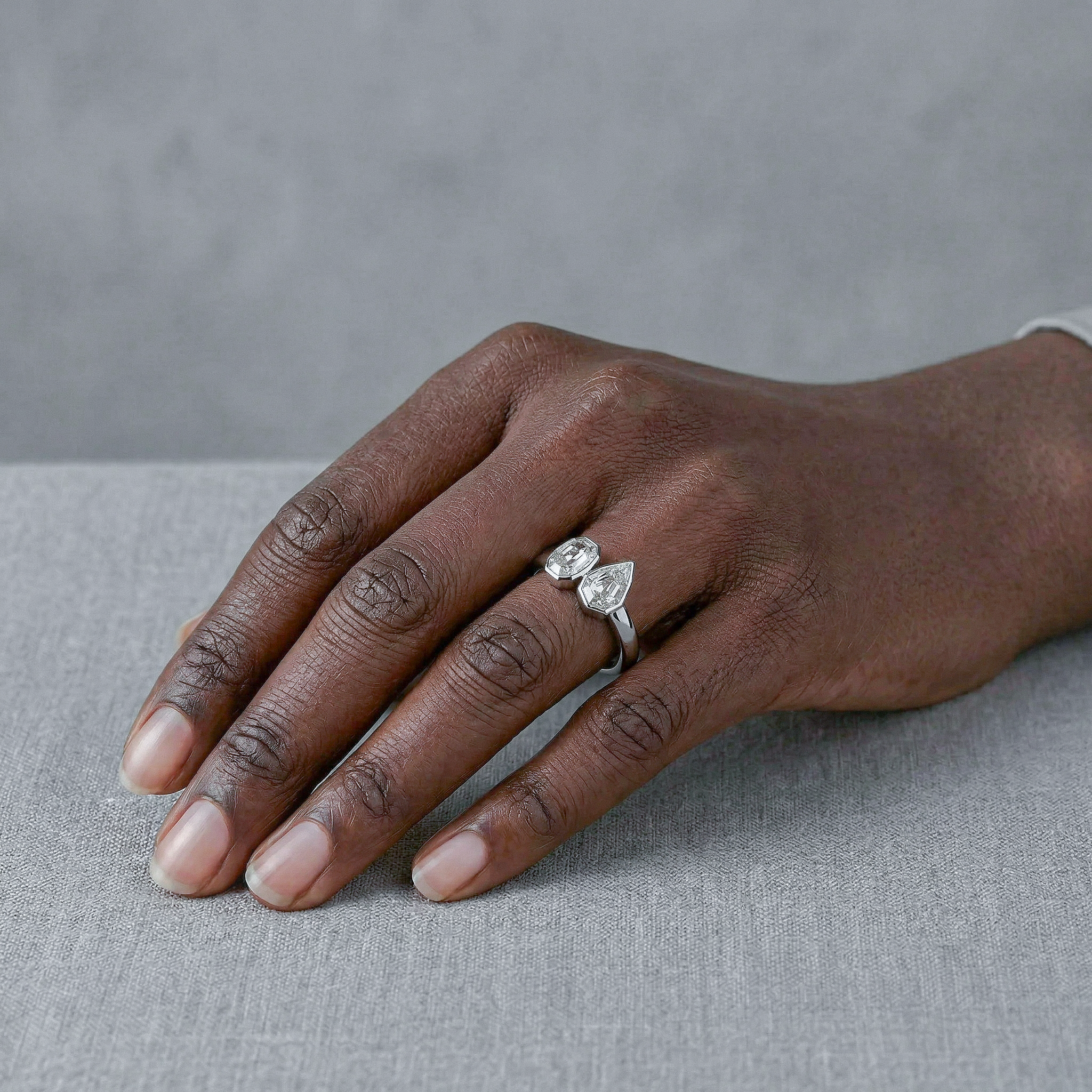 Hand wearing a white gold ring with two diamonds on a gray background