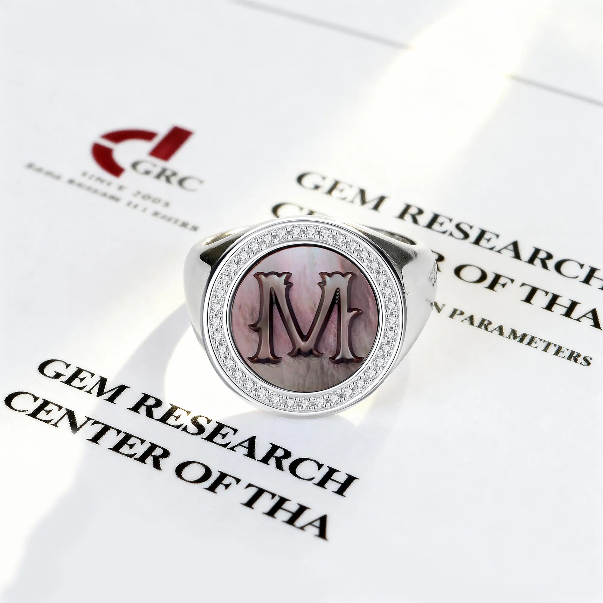 Silver ring with a mother of pearl and 'M' initials on a Gem Research Center of The document.