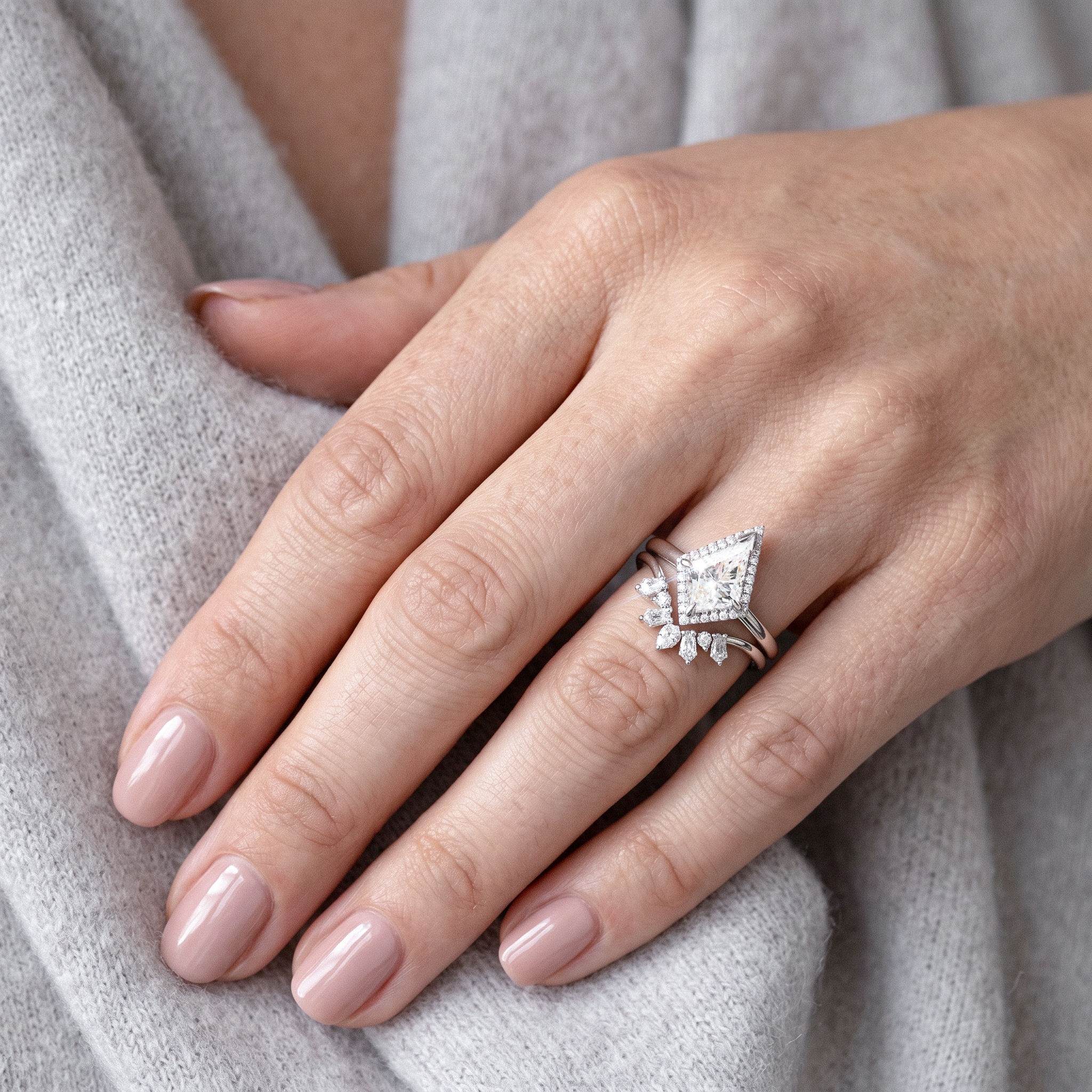 Hand wearing kite cut diamond ring set on a light gray fabric background