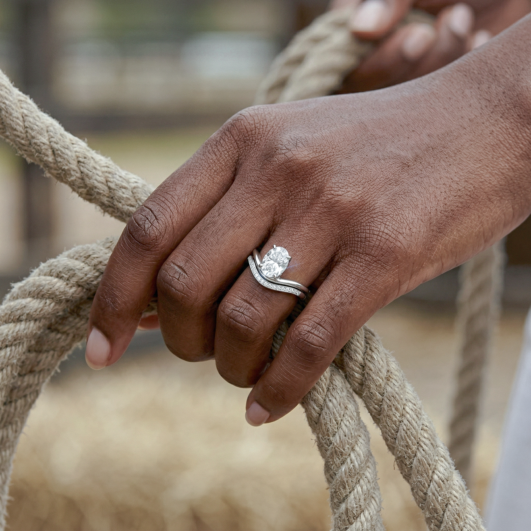 Hand holding a rope with a oval diamond ring set on a blurred natural background