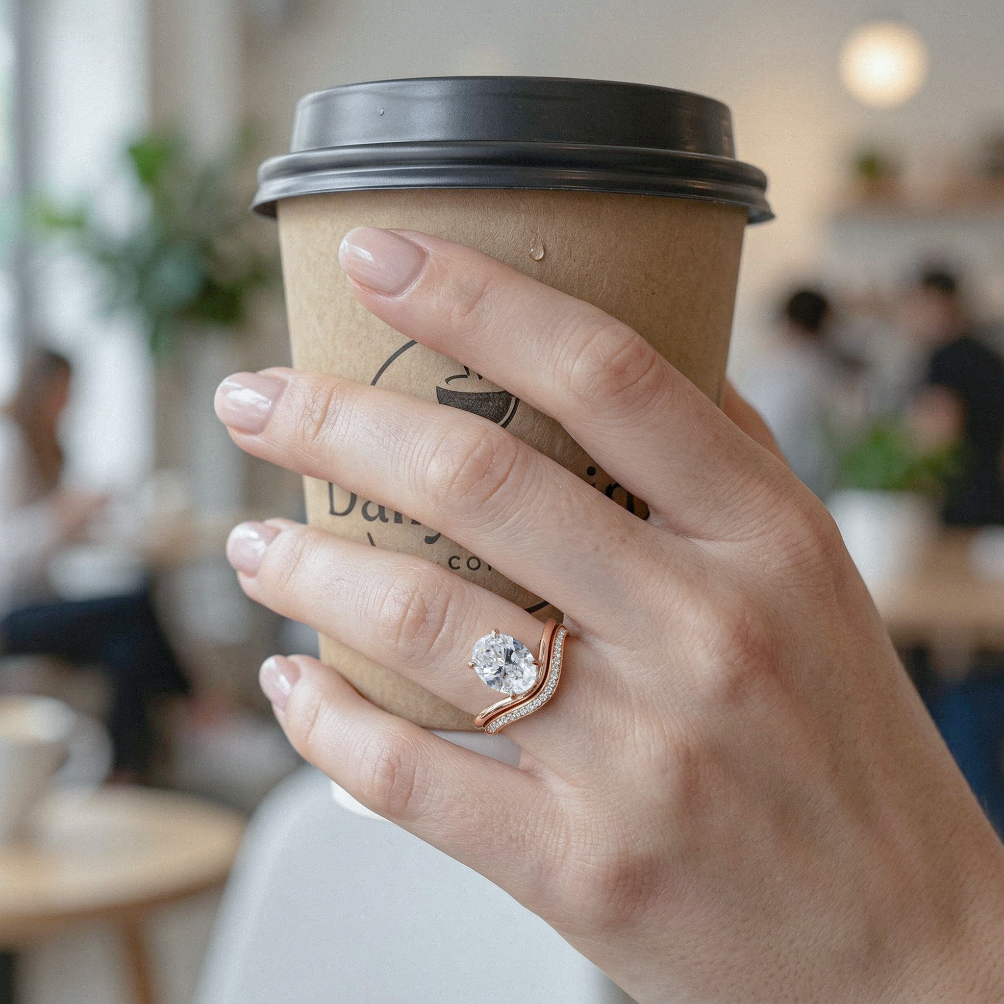 Hand holding a coffee cup with a oval diamond ring set on a blurred cafe background