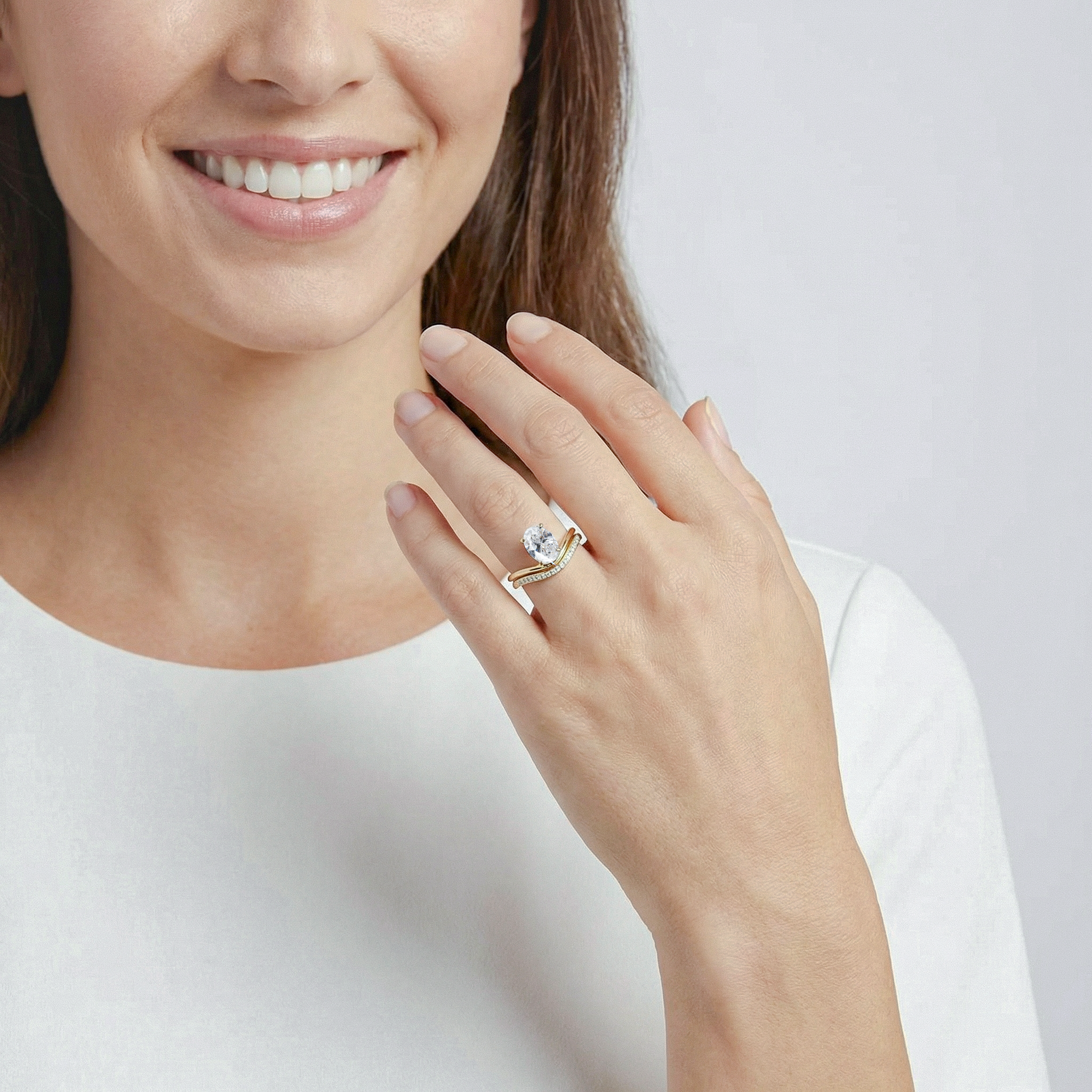 Woman wearing gold ring set with oval diamond on a plain background
