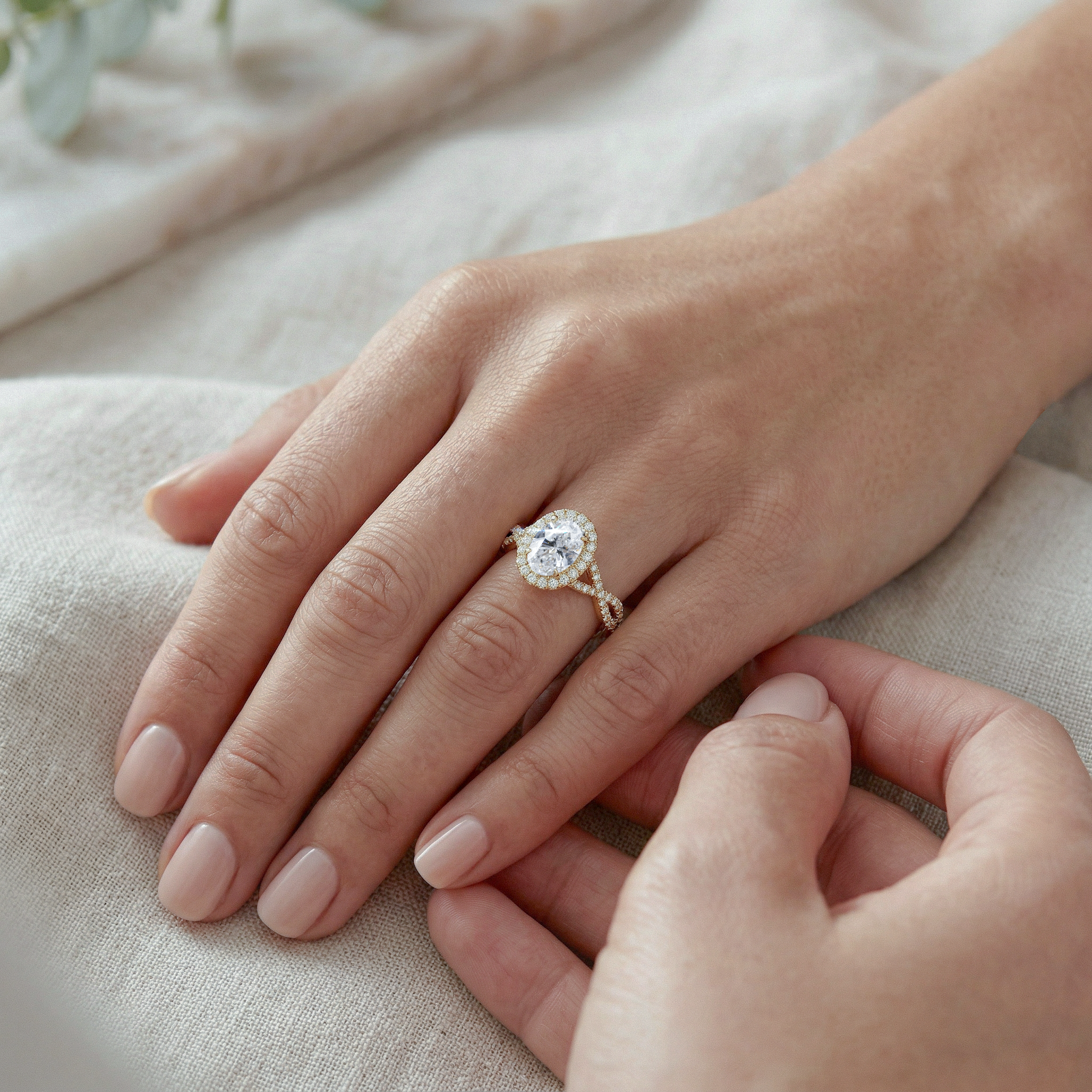 Close-up of a hand wearing a twisted oval diamond ring on a light fabric background