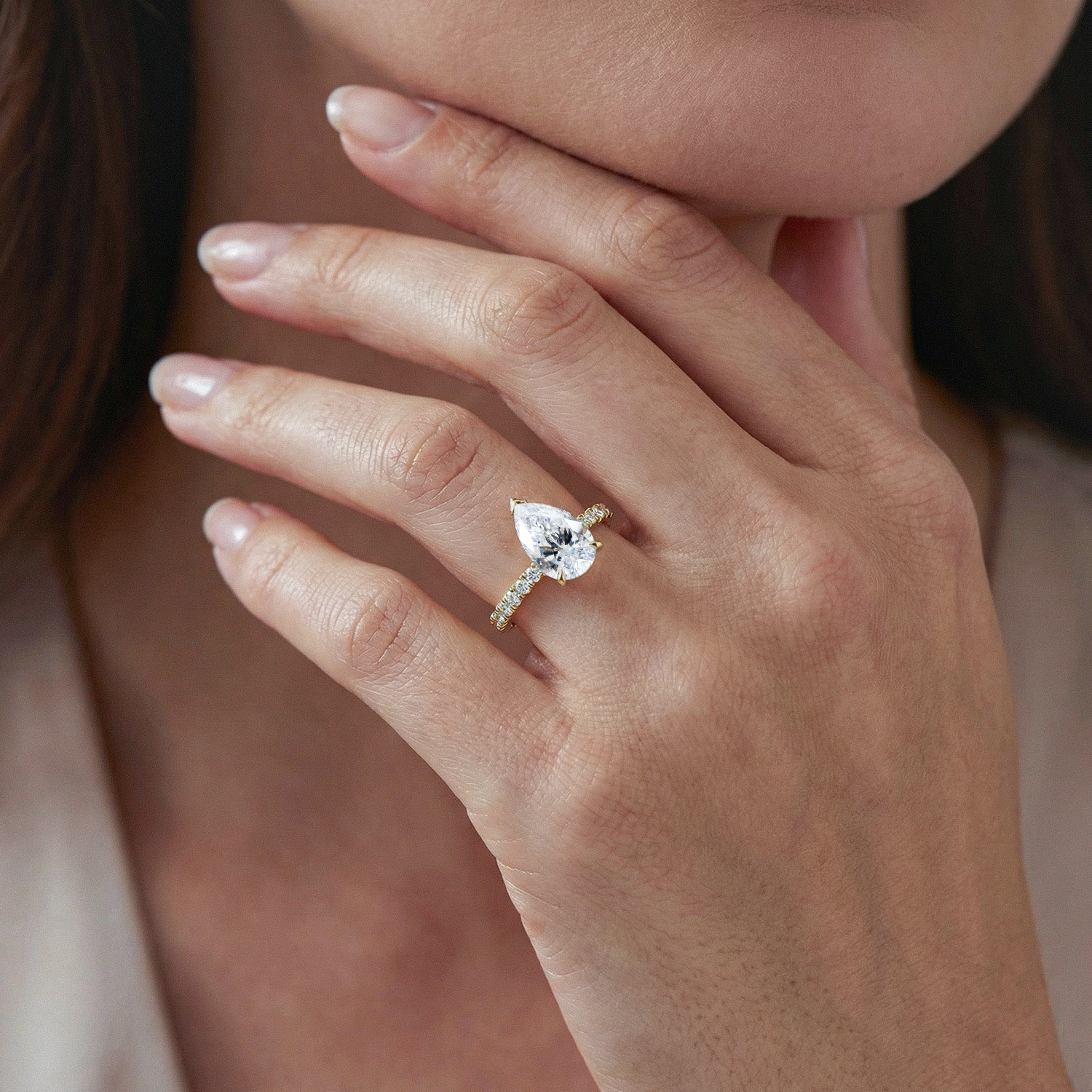 Close-up of a hand wearing a pear diamond ring with a blurred background