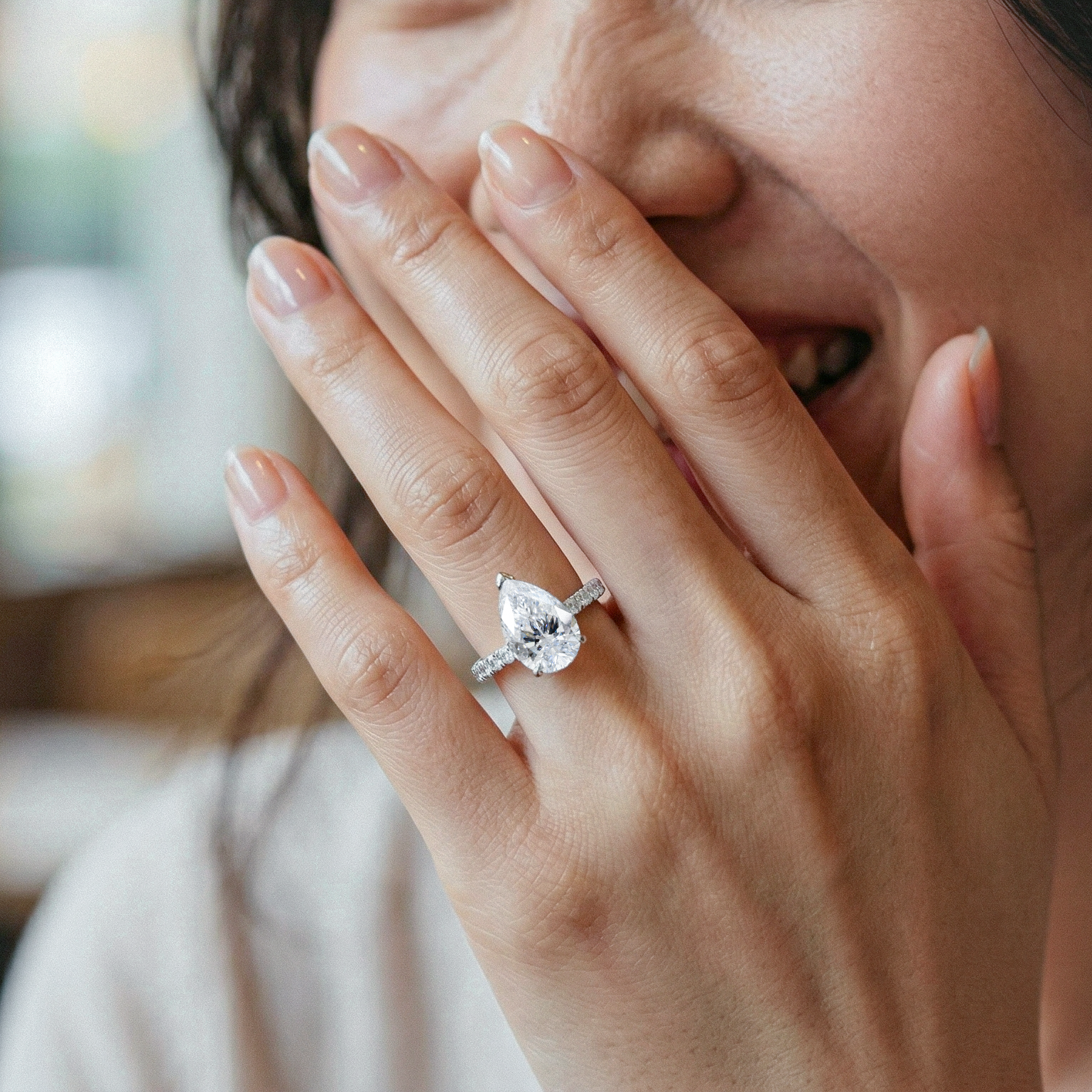 Close-up of a hand with a pear diamond ring, covering the face.