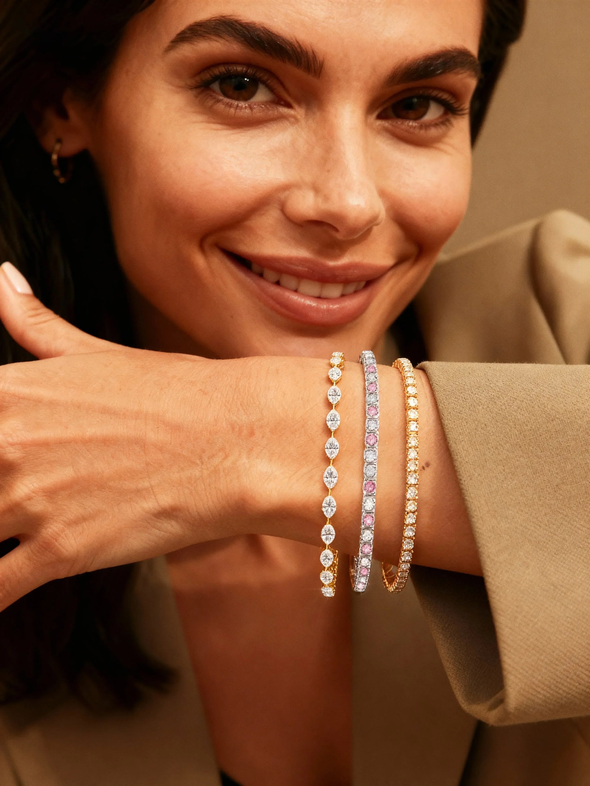 Smiling woman showcasing three layered tennis bracelets in white gold, pink, and yellow gold