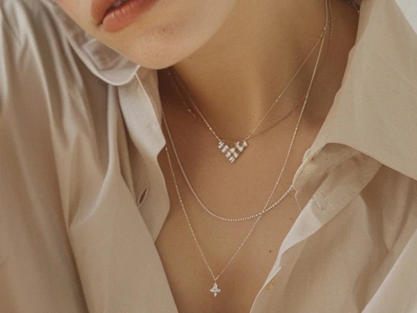Close-up of a gold necklace with a two marquise-cut diamond pendant, worn over a light-colored blouse