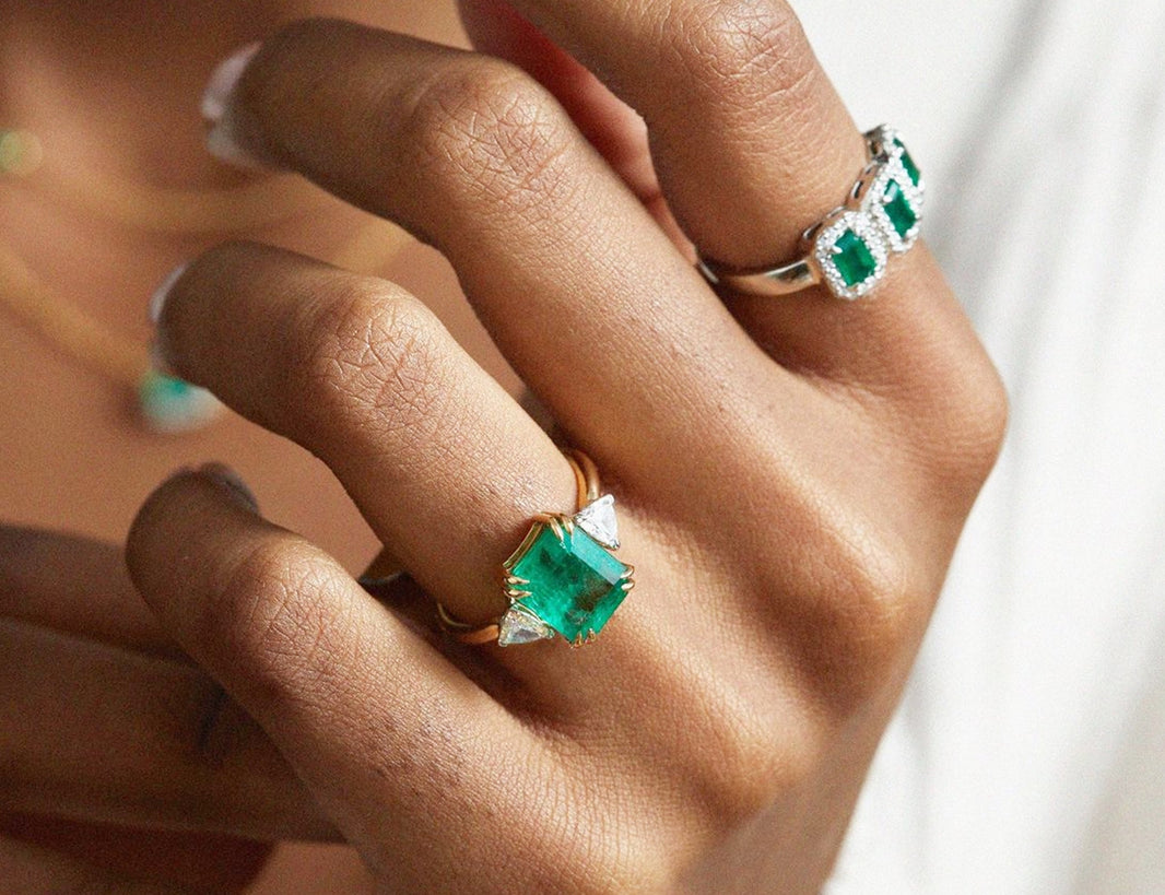A person's hand with white nail polish wearing two gold rings with green gemstones