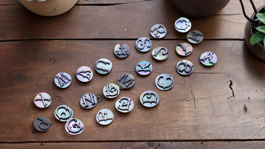 Collection of mother of pearl circular inlays featuring various alphabet letters and symbols arranged on a wooden surface, showcasing the material's natural iridescent colors