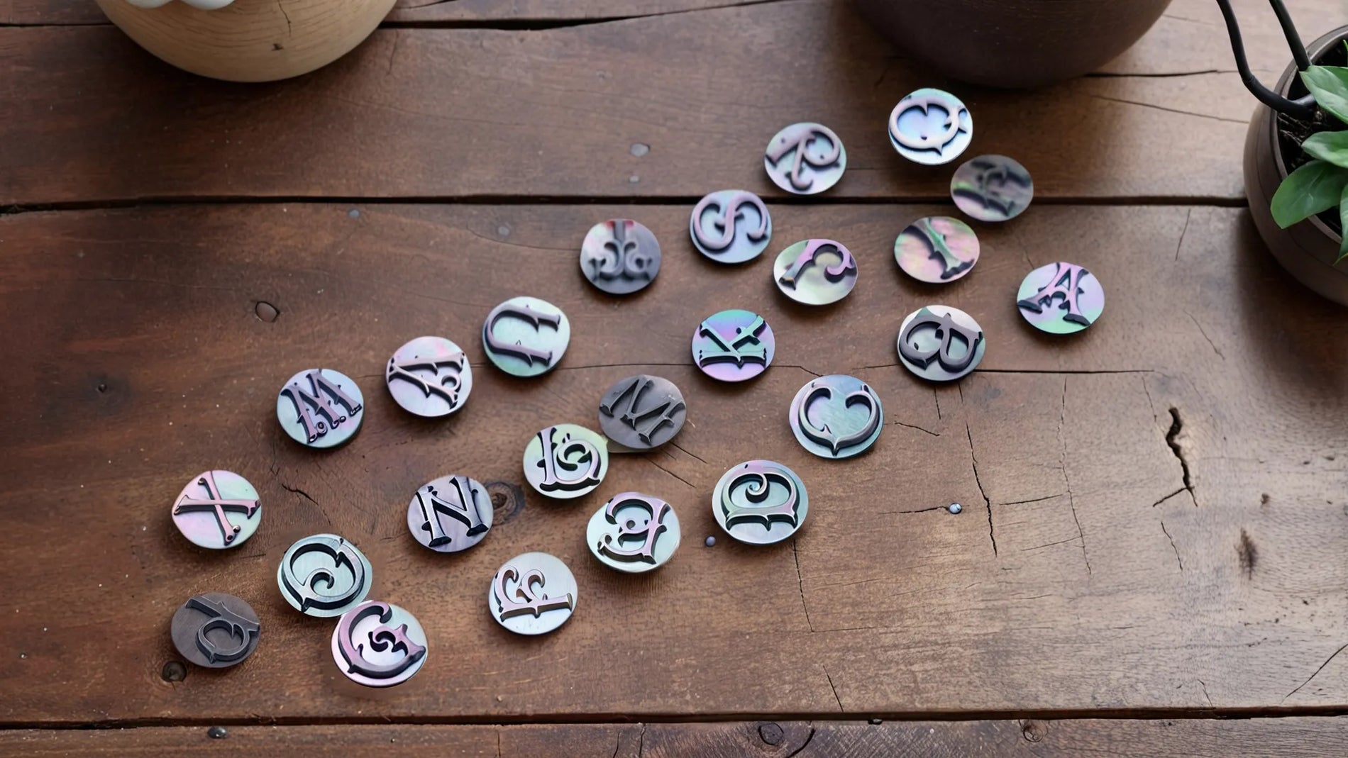 Collection of mother of pearl circular inlays featuring various alphabet letters and symbols arranged on a wooden surface, showcasing the material's natural iridescent colors