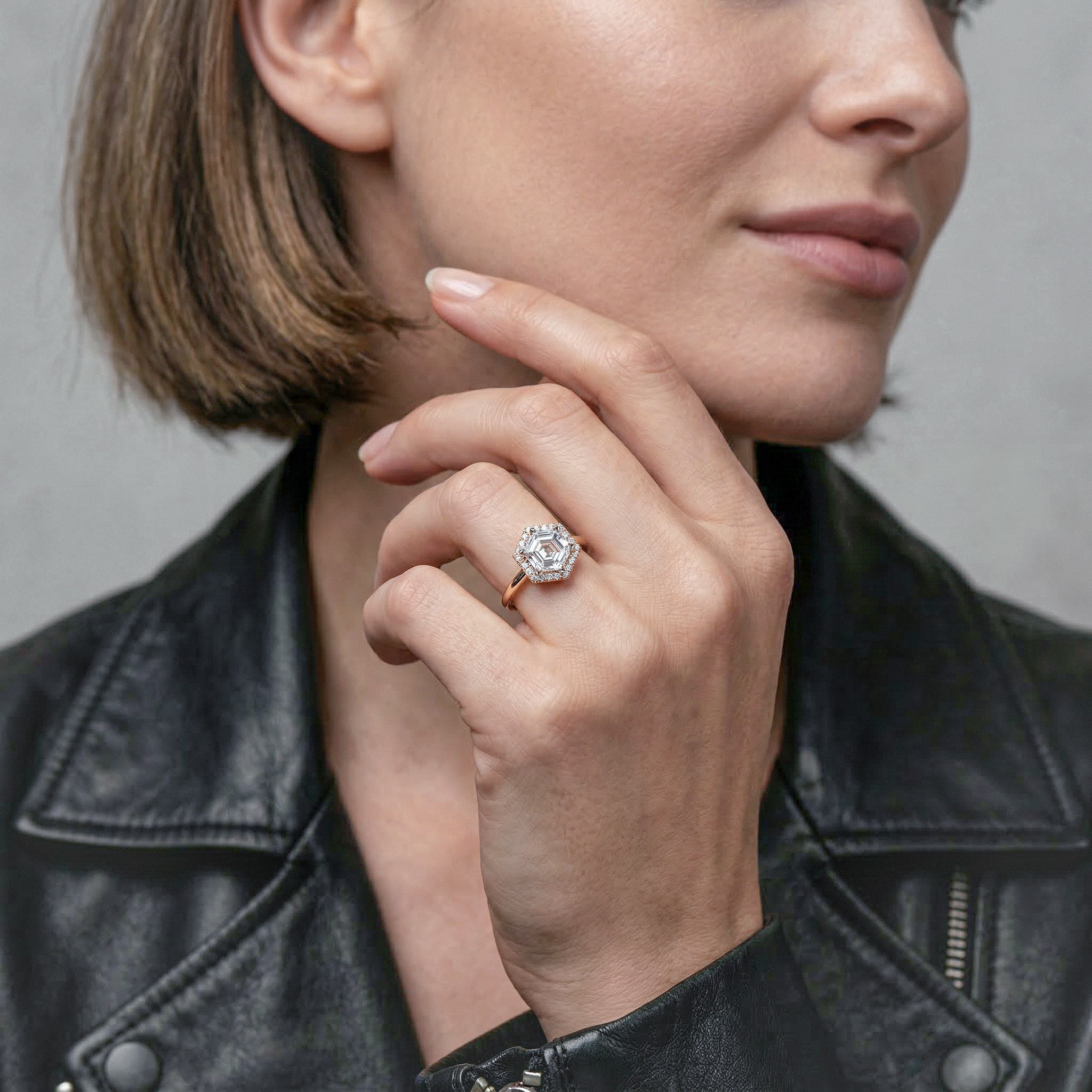 Close-up of a person wearing a halo hecagon diamond ring on a gray background