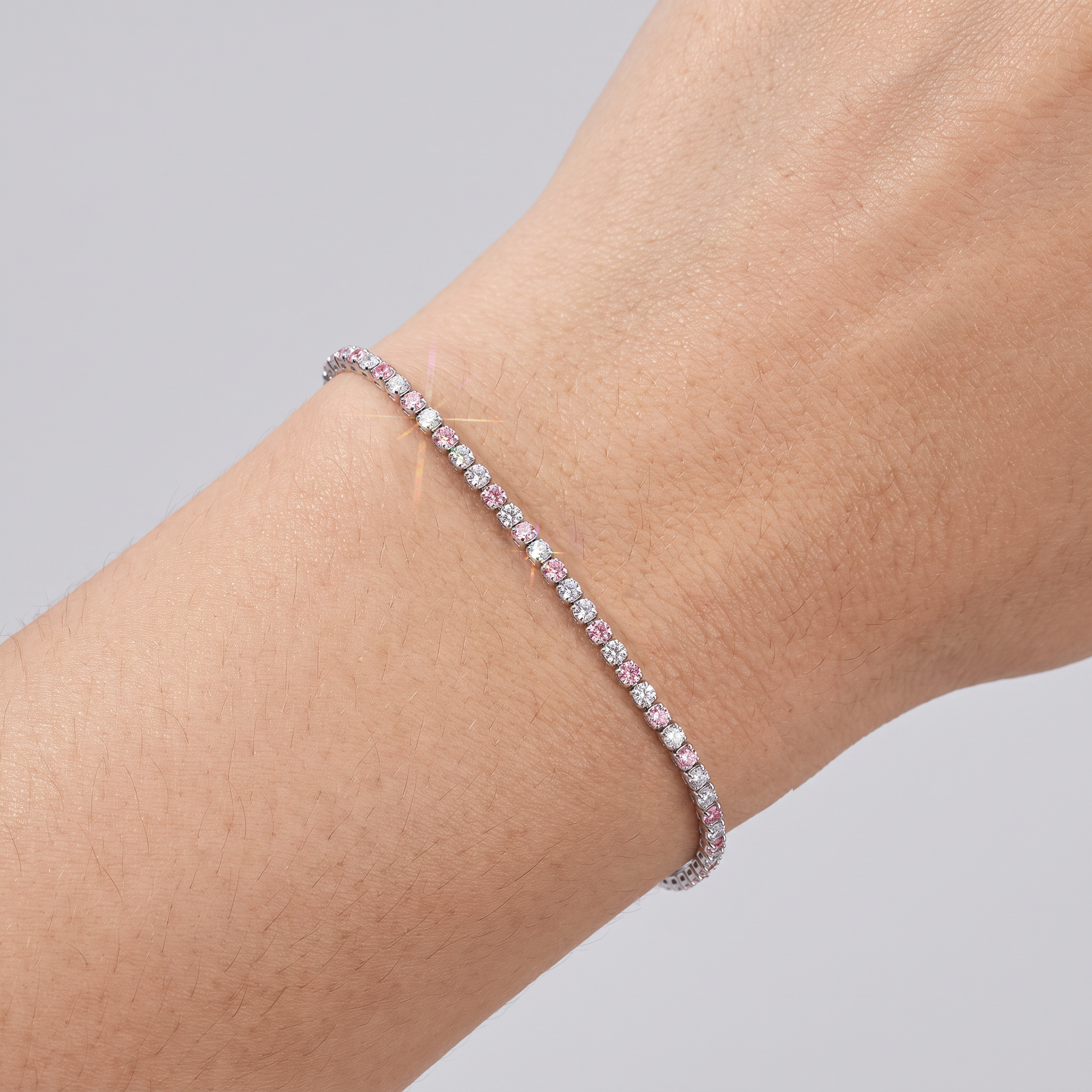 Close-up of a white gold tennis bracelet with alternating white and pink lab-grown diamonds on a wrist.