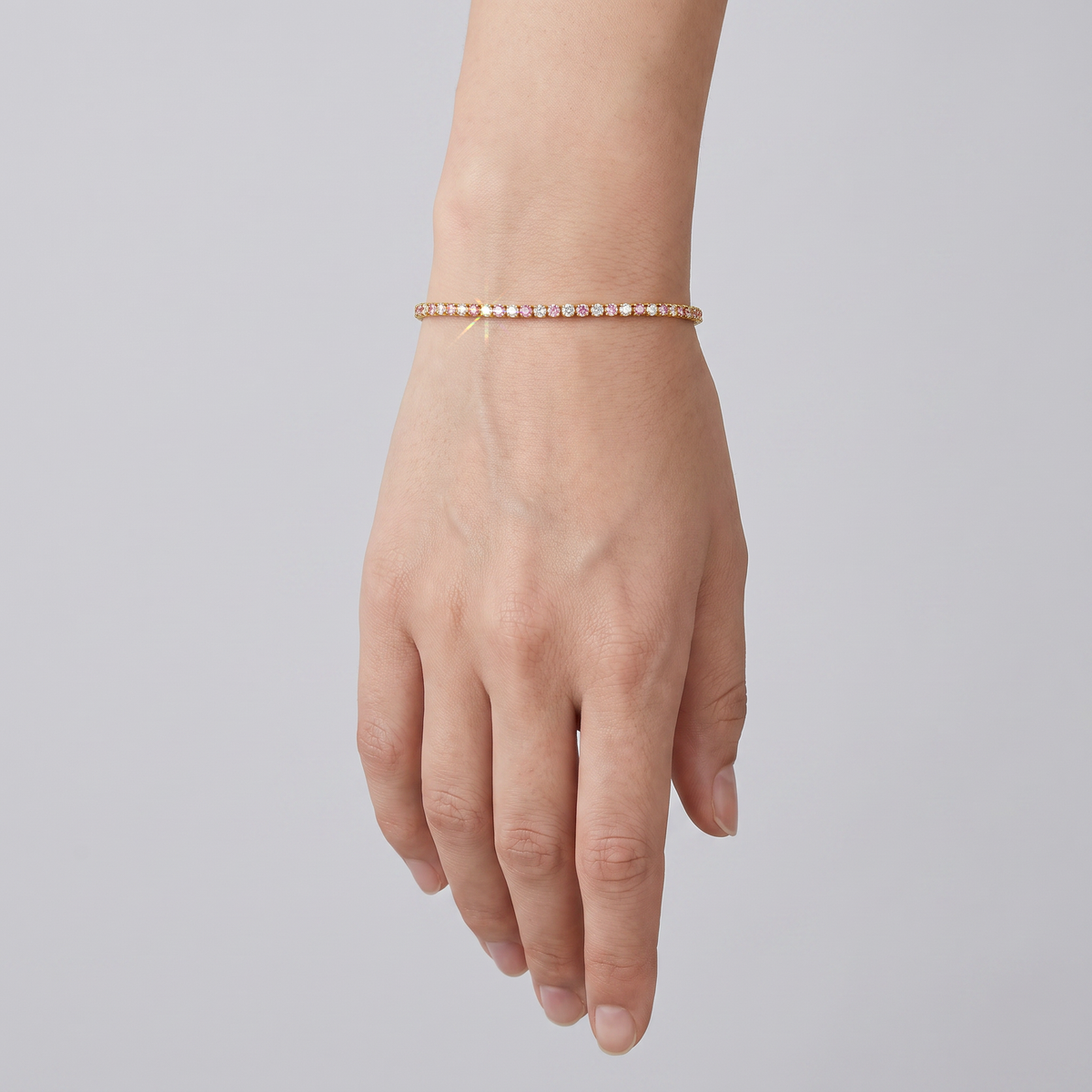 Yellow gold tennis bracelet with alternating white and pink lab-grown diamonds shown on a wrist.