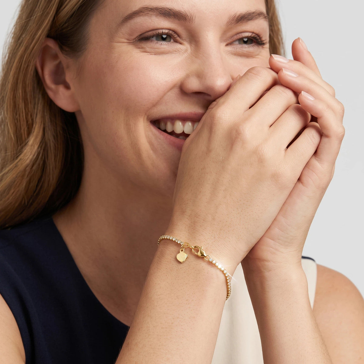 Model wearing a yellow gold lab-grown diamond tennis bracelet with an adjustable chain and heart charm.