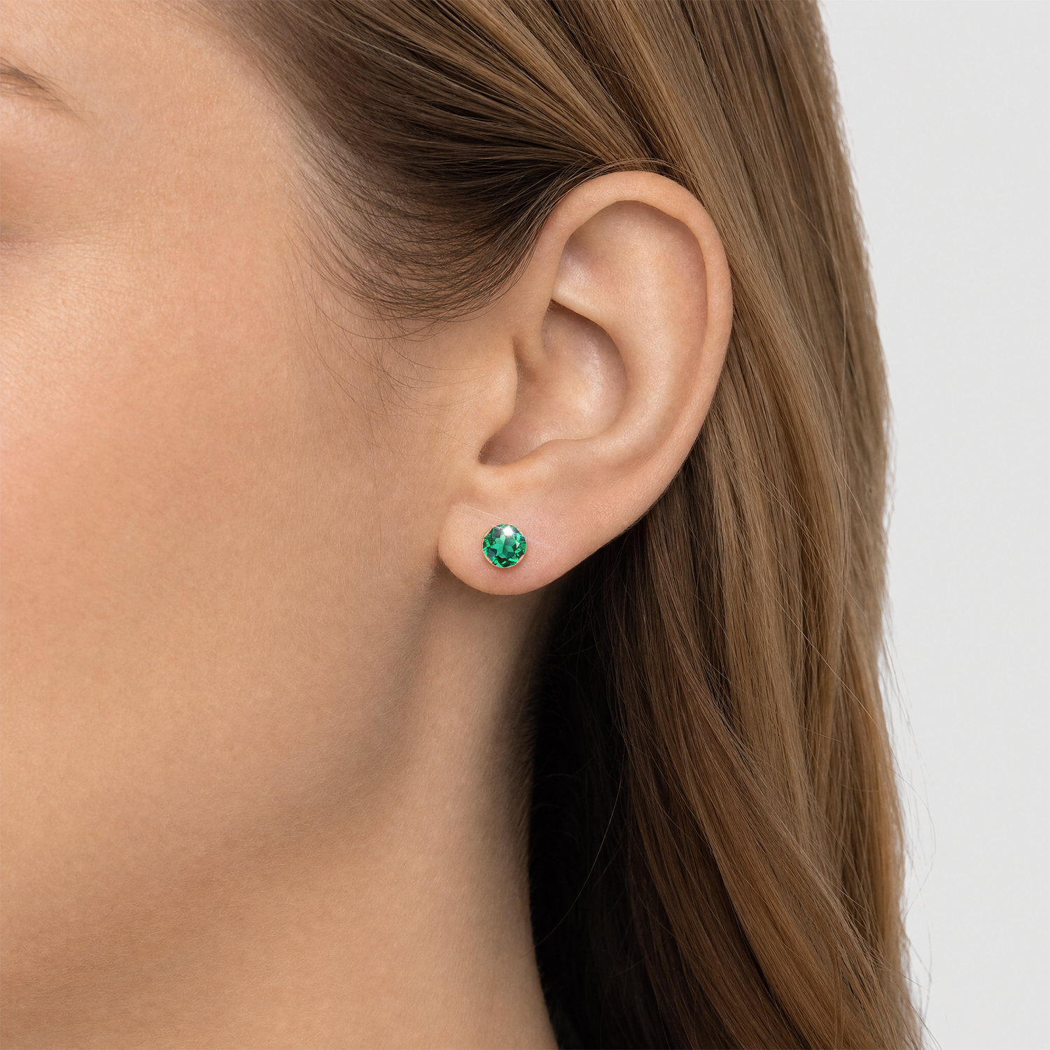 Two sizes of round lab-grown emerald stud earrings in rose gold worn together on the ear.