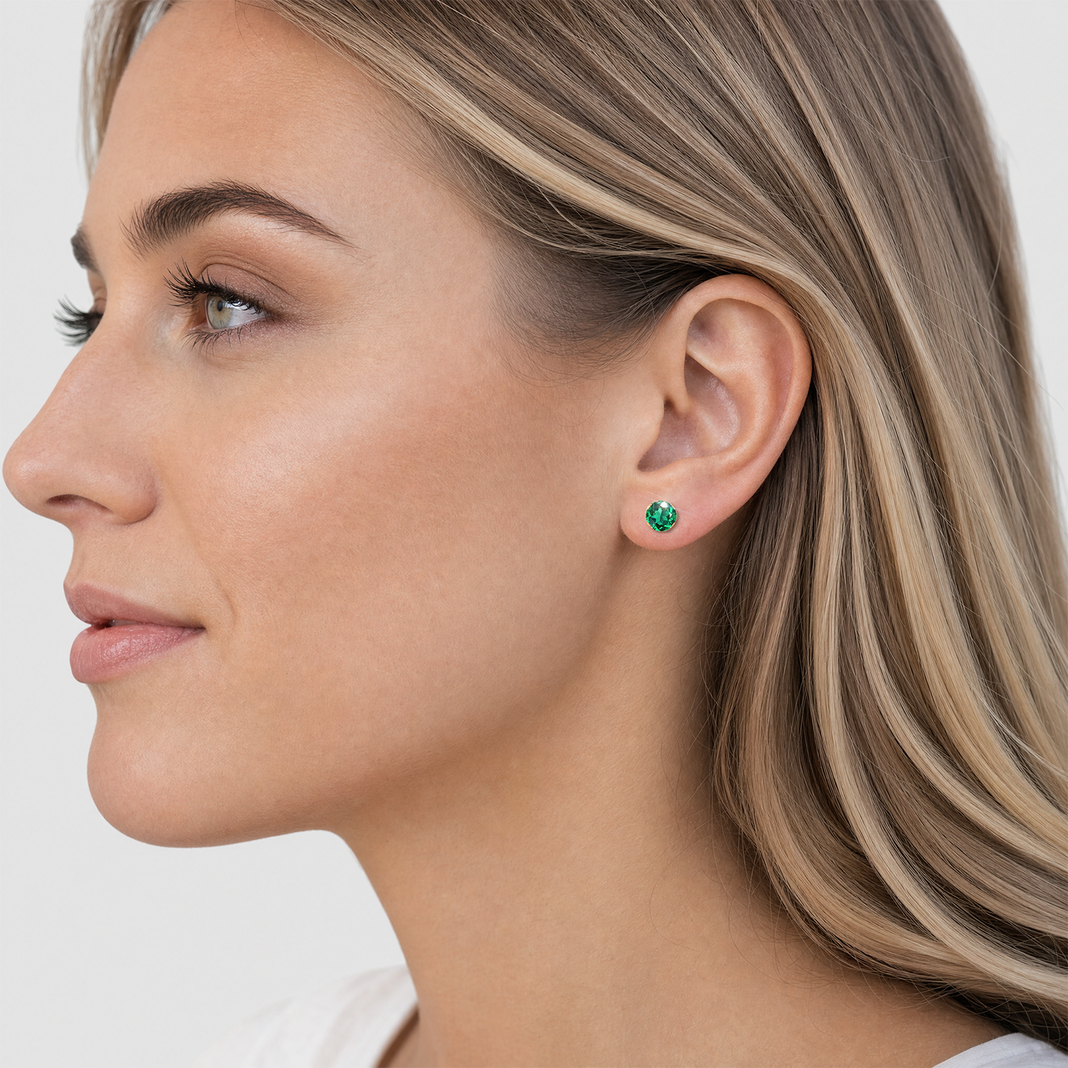 Round lab-grown emerald stud earring in yellow gold worn on the earlobe.