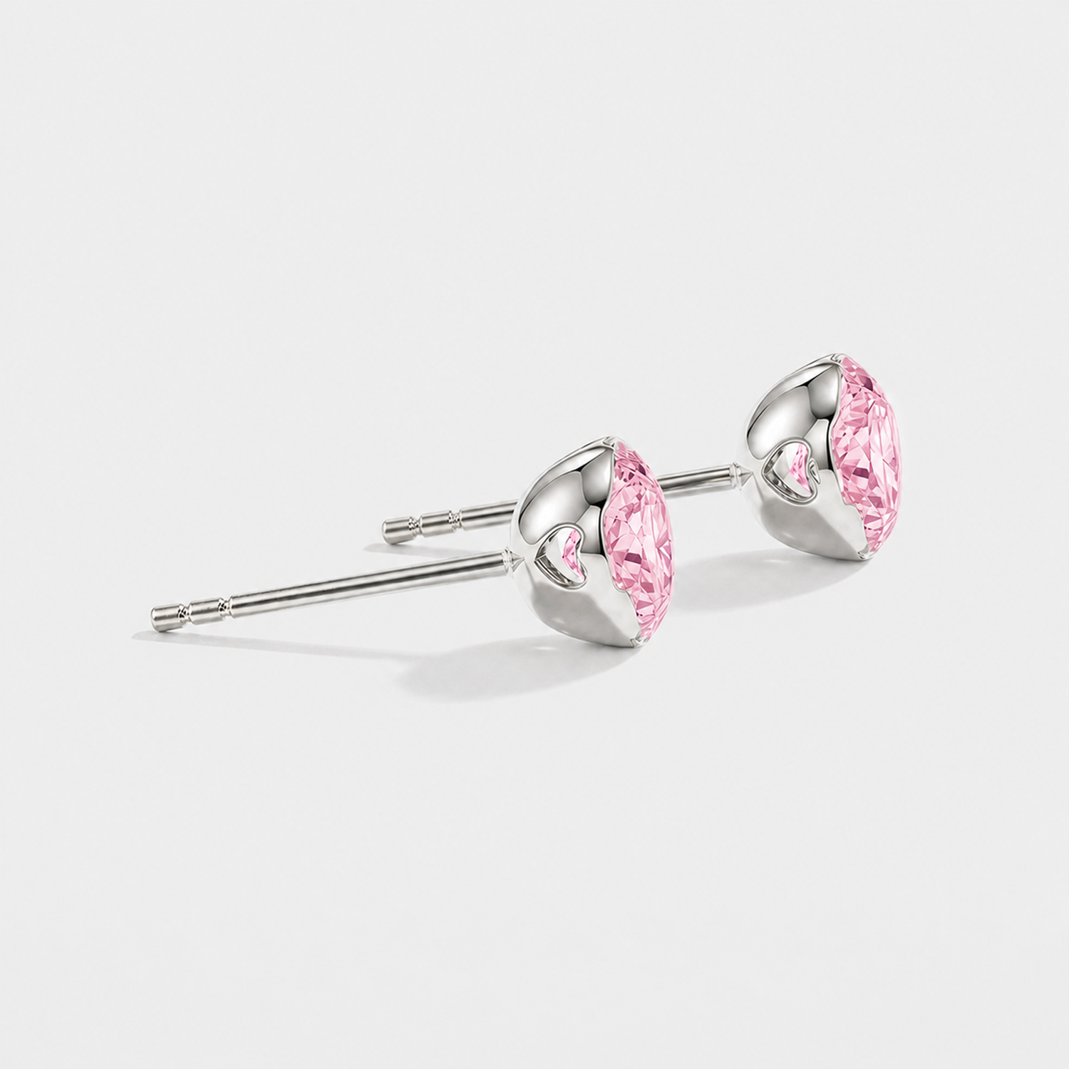Side profile of round pink lab-grown diamond stud earrings showing heart-shaped openings in the white gold settings.