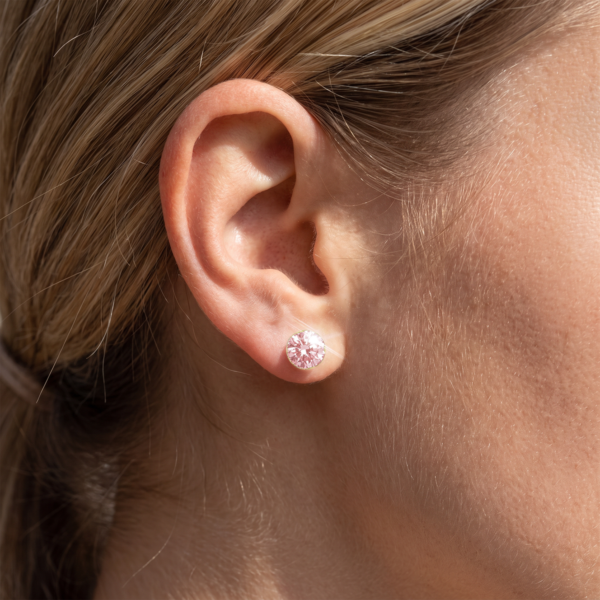 Round pink lab-grown diamond stud earring in yellow gold worn on the earlobe.