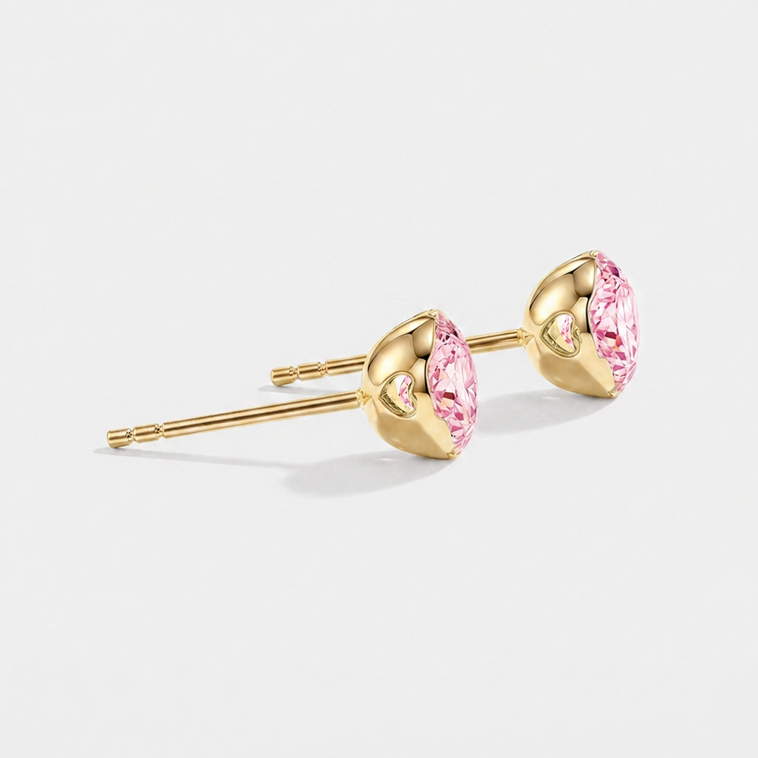 Side view of round pink lab-grown diamond stud earrings showing heart-shaped openings in the yellow gold settings.