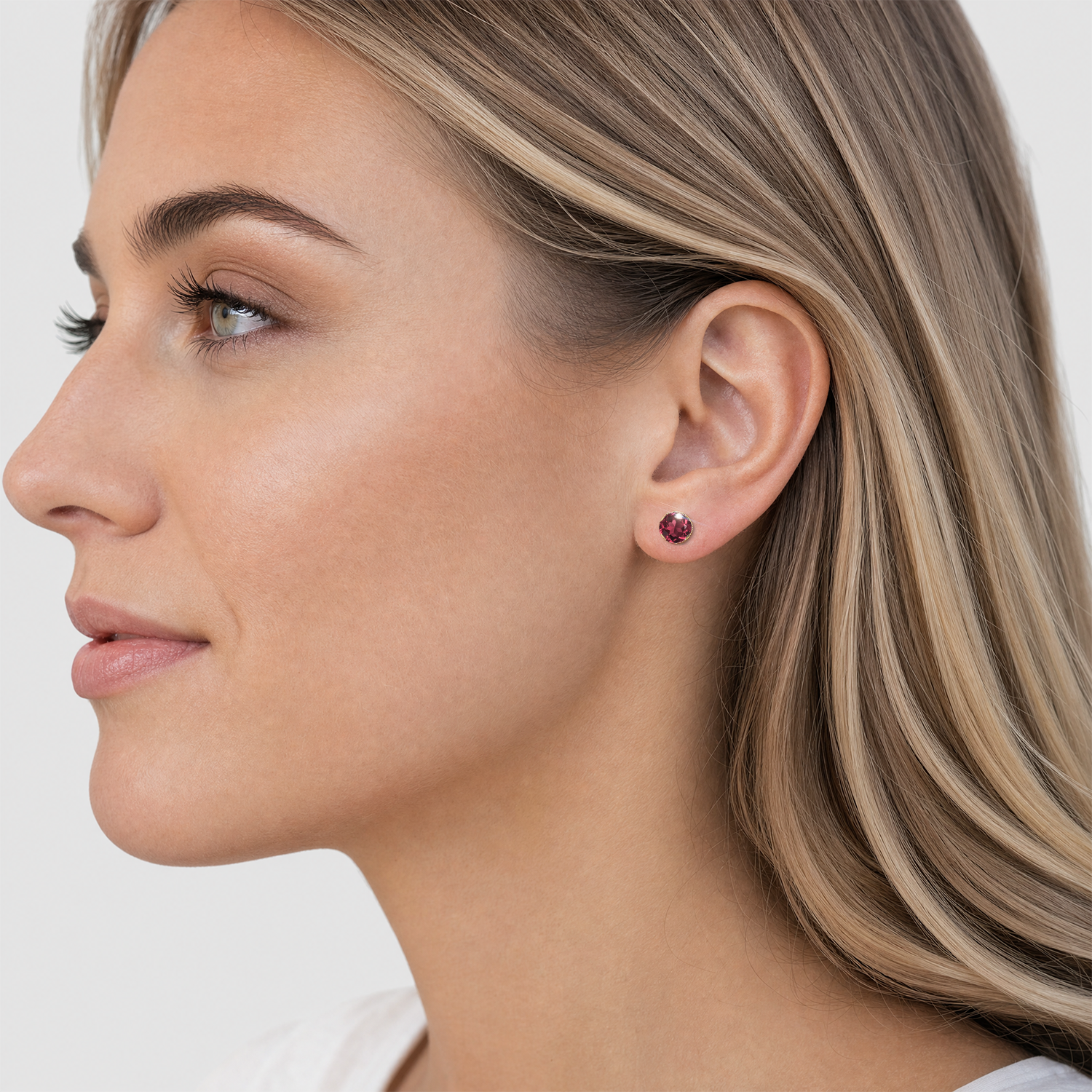 Round lab-grown ruby stud earring in yellow gold worn on the earlobe.