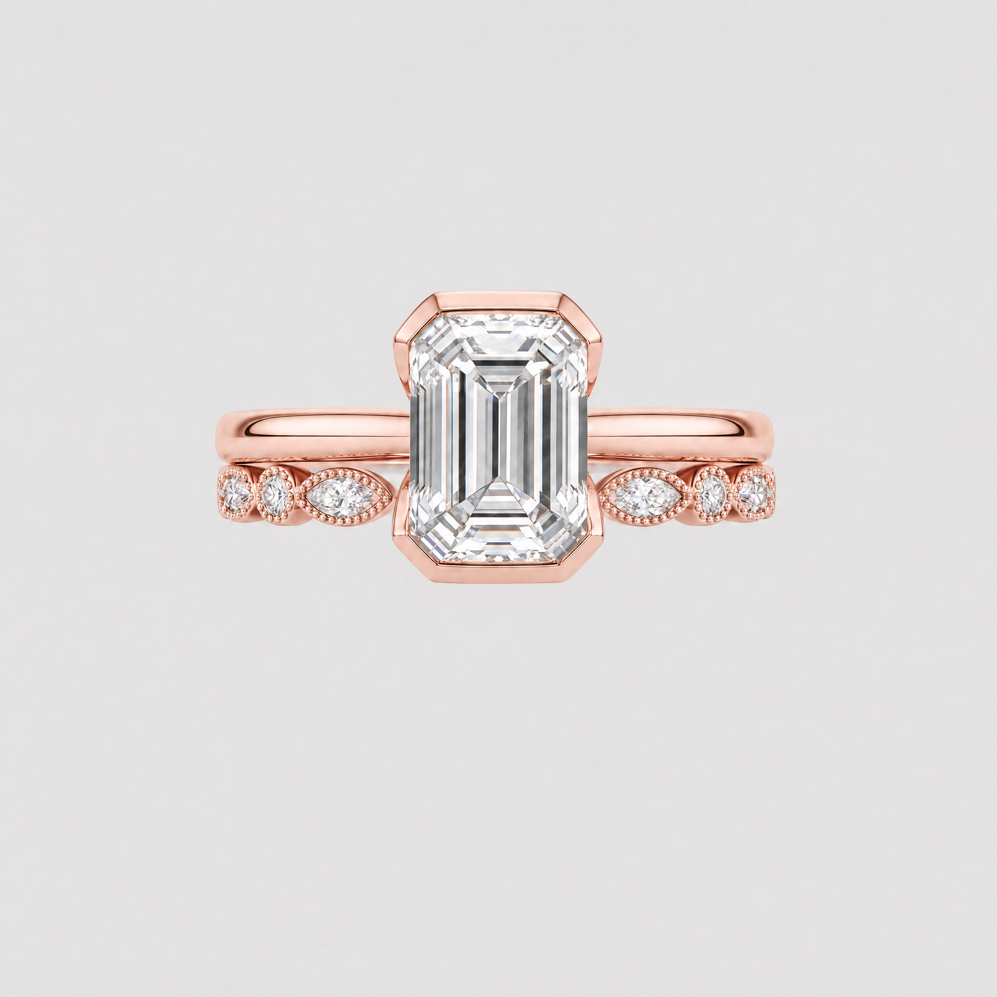 Front view of an emerald-cut two-ring bridal set in rose gold with a marquise-and-round stone band.