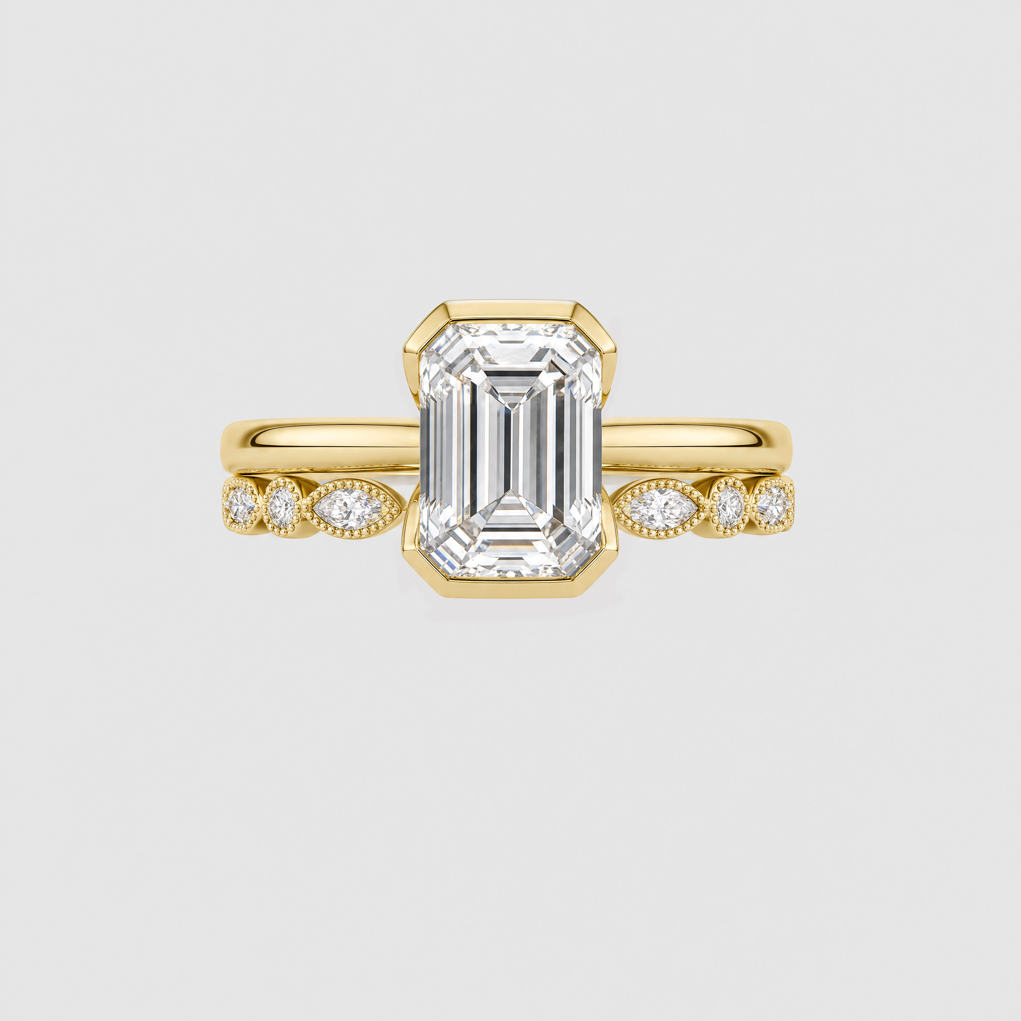Front view of an emerald-cut two-ring bridal set in yellow gold with a marquise-and-round stone band.