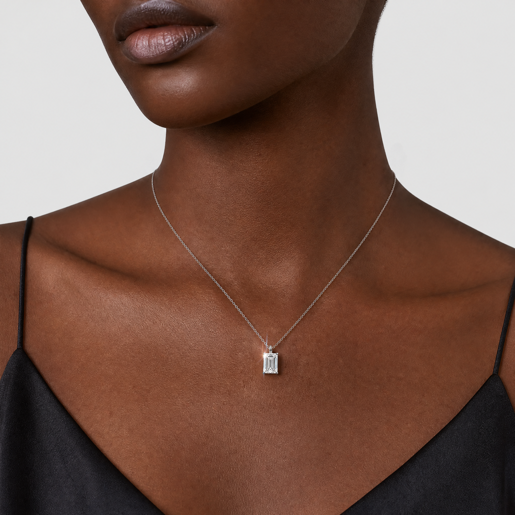 White-gold emerald-cut pendant worn on a fine chain in a front neck view.