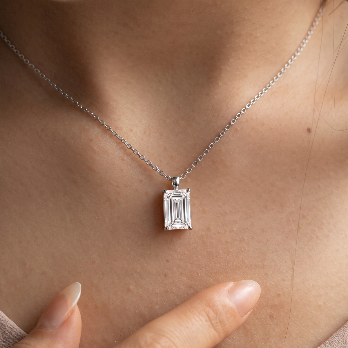 Close-up of a white-gold emerald-cut pendant worn on a fine chain.