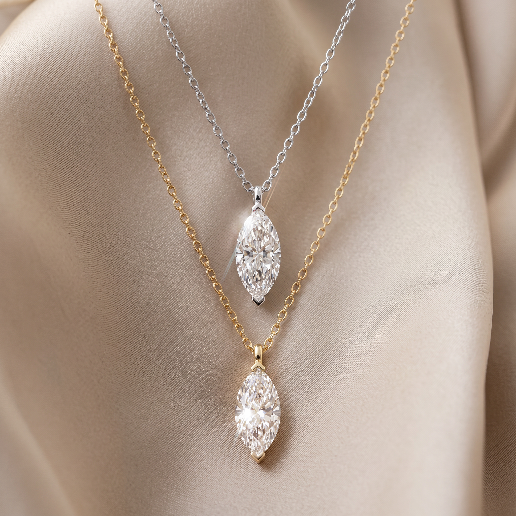 White- and yellow-gold marquise-cut pendants displayed on fine chains against neutral fabric.