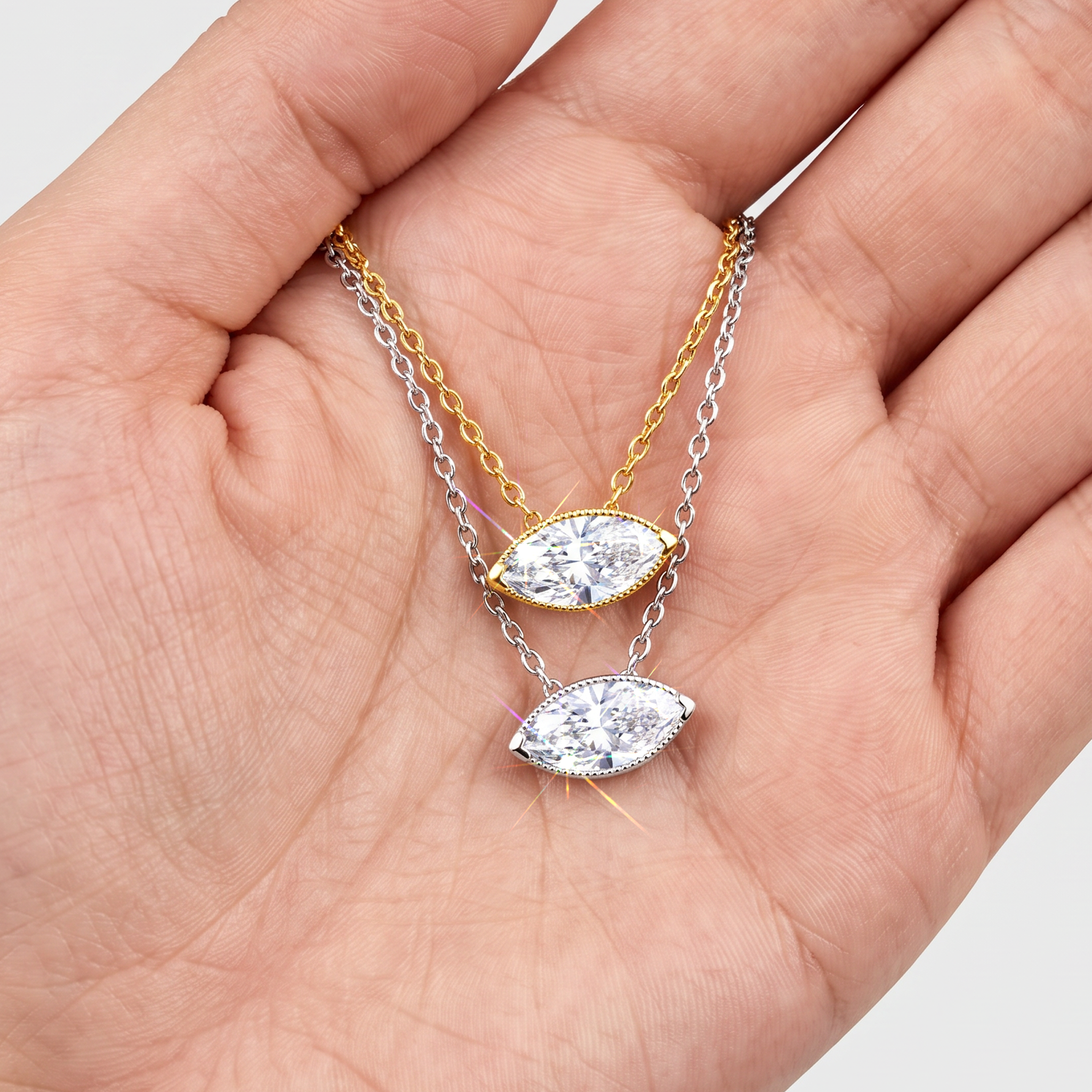 Yellow and white gold marquise-cut diamond pendants displayed on fine chains in a hand.