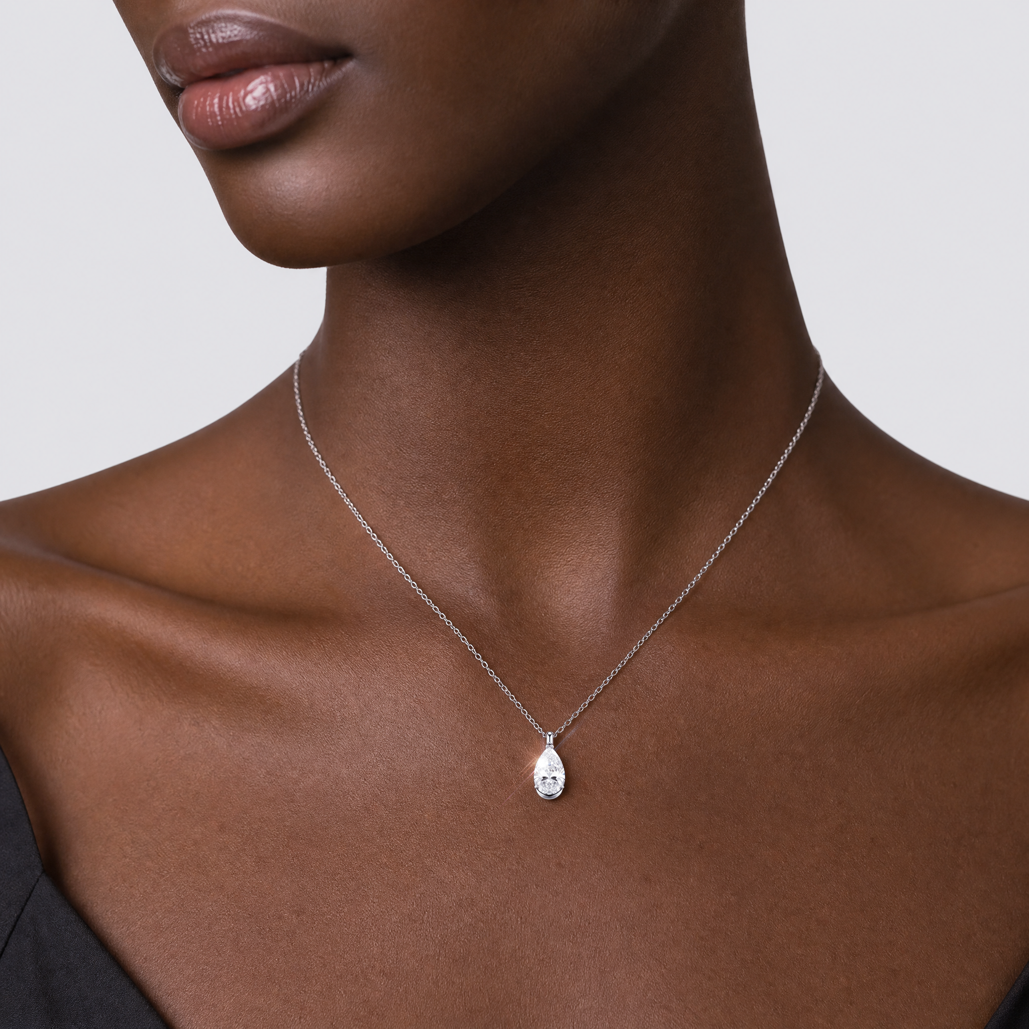Model wearing a pear-cut diamond pendant in white gold on a fine chain.