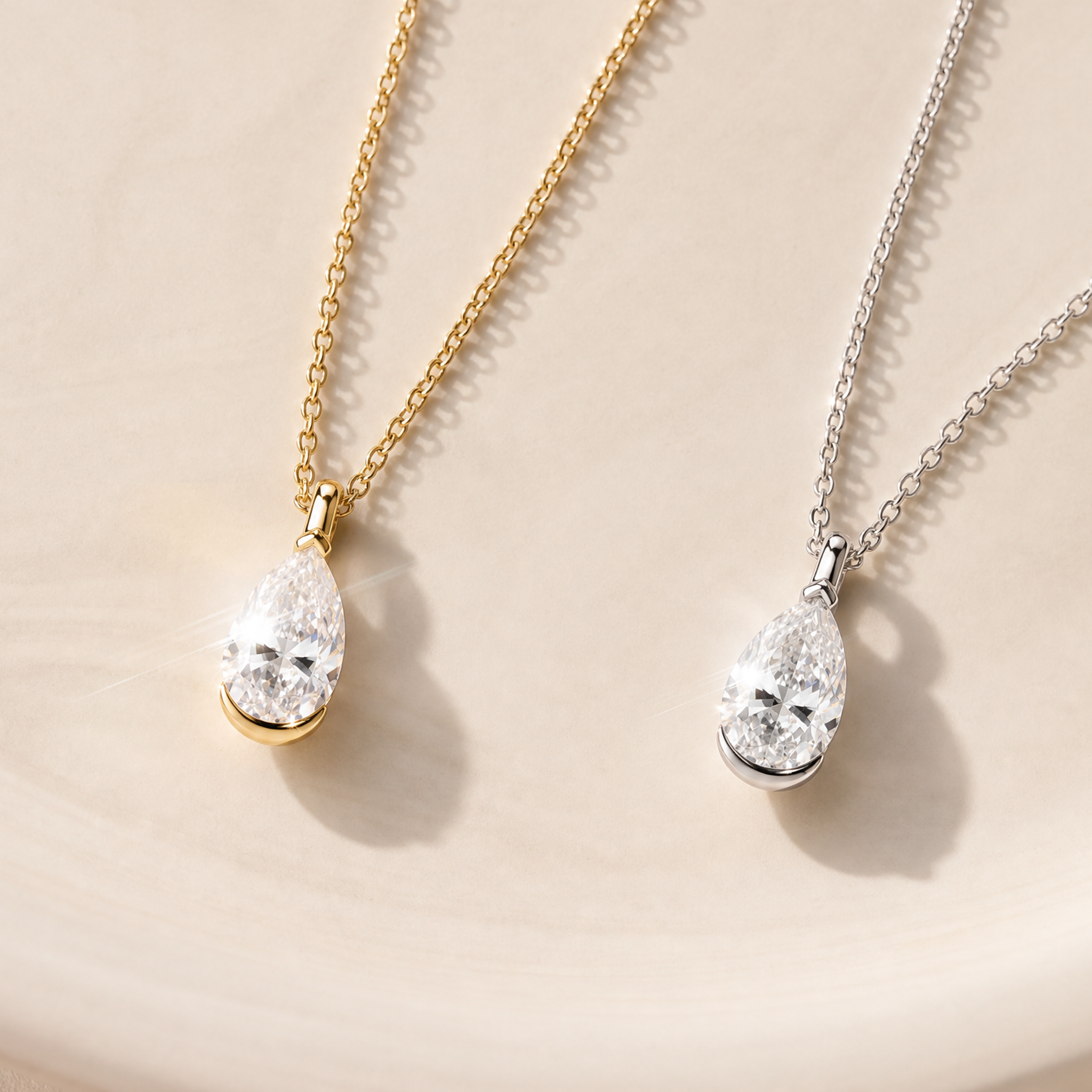 White and yellow gold pear-cut diamond pendants displayed on fine chains in a styled scene.